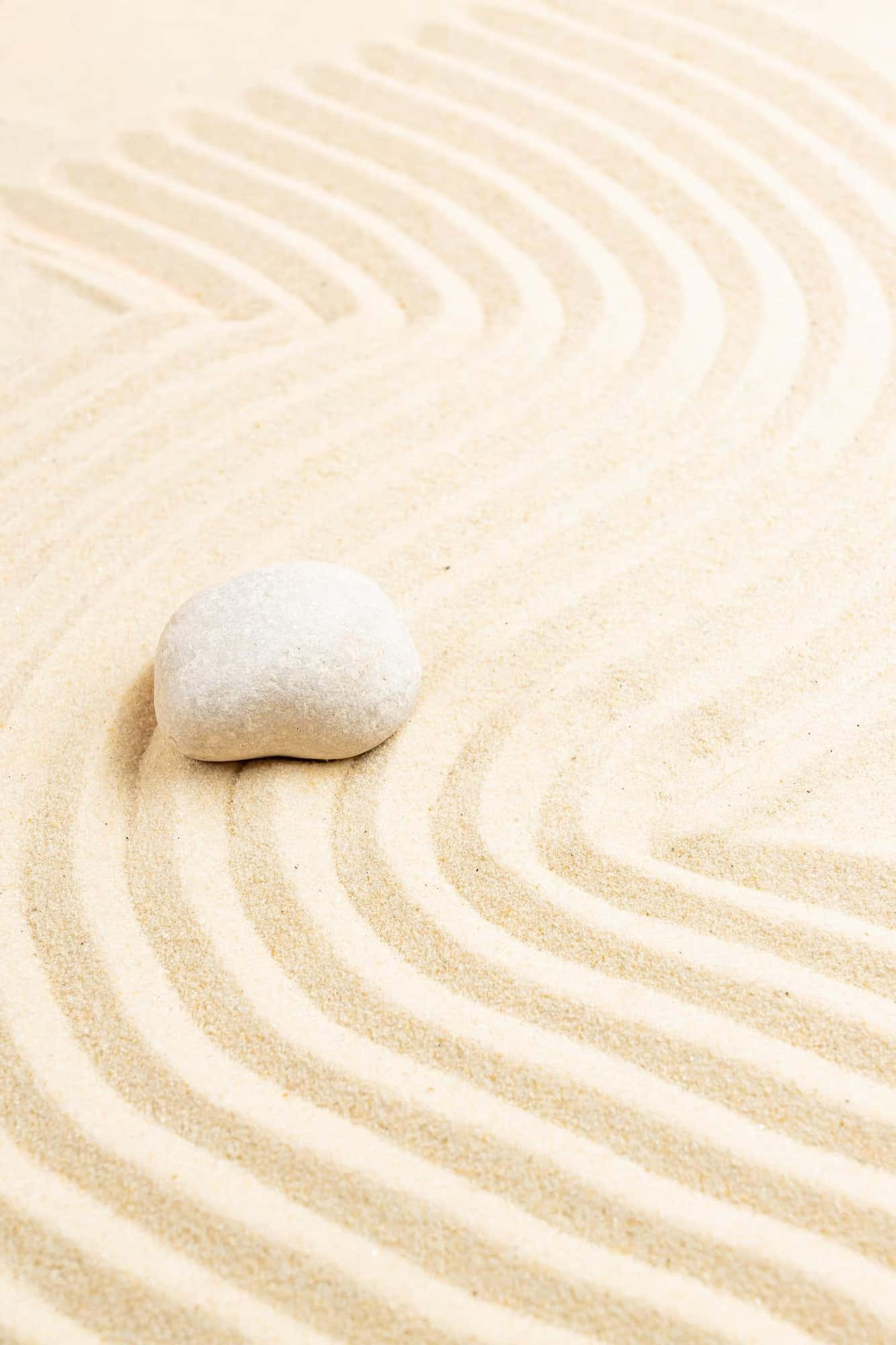 Stone 桌布 壁紙 — 一塊光滑的石頭安放在精心耙過的沙子上，在極簡禪園中形成柔和的同心波紋。