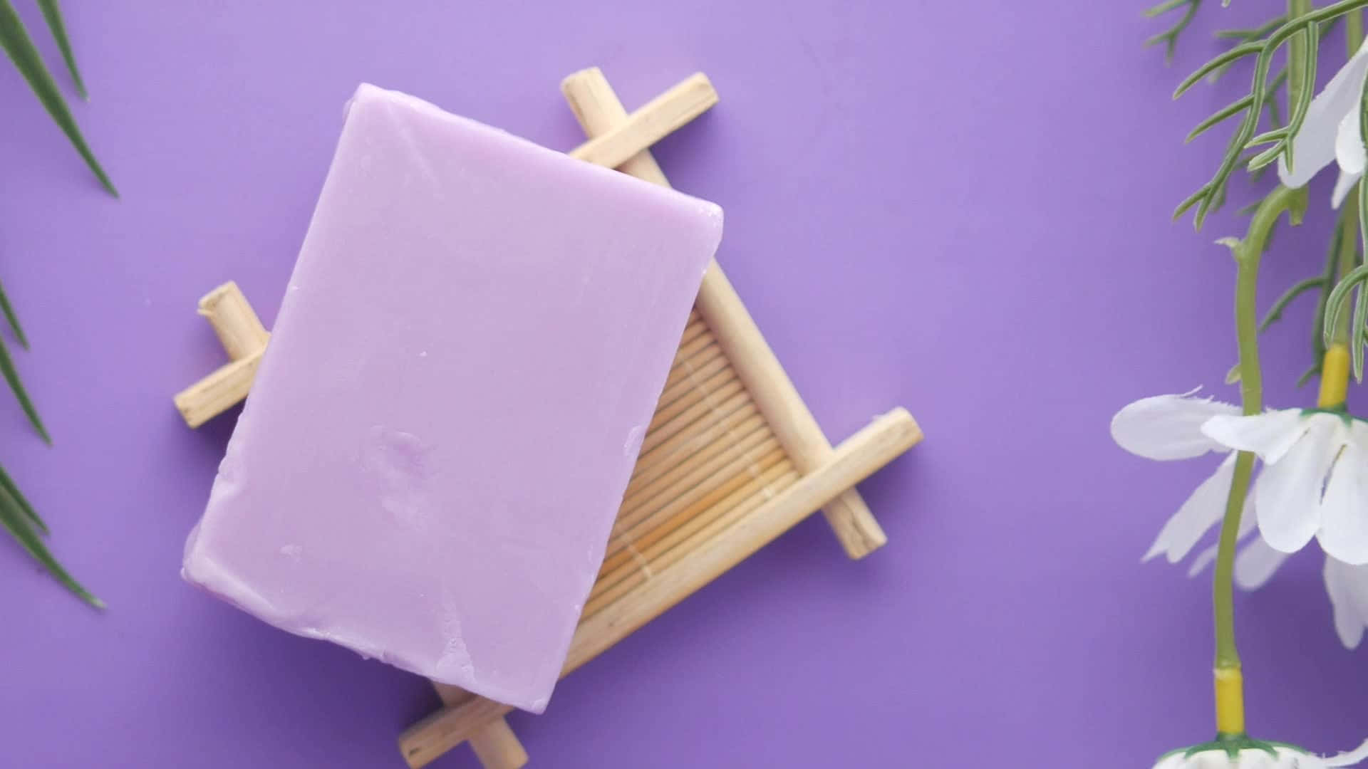 bath 桌布 壁紙 — 一塊光滑的薰衣草肥皂放在木架上，背景是充滿活力的紫色，配有白色花朵和綠色葉子。