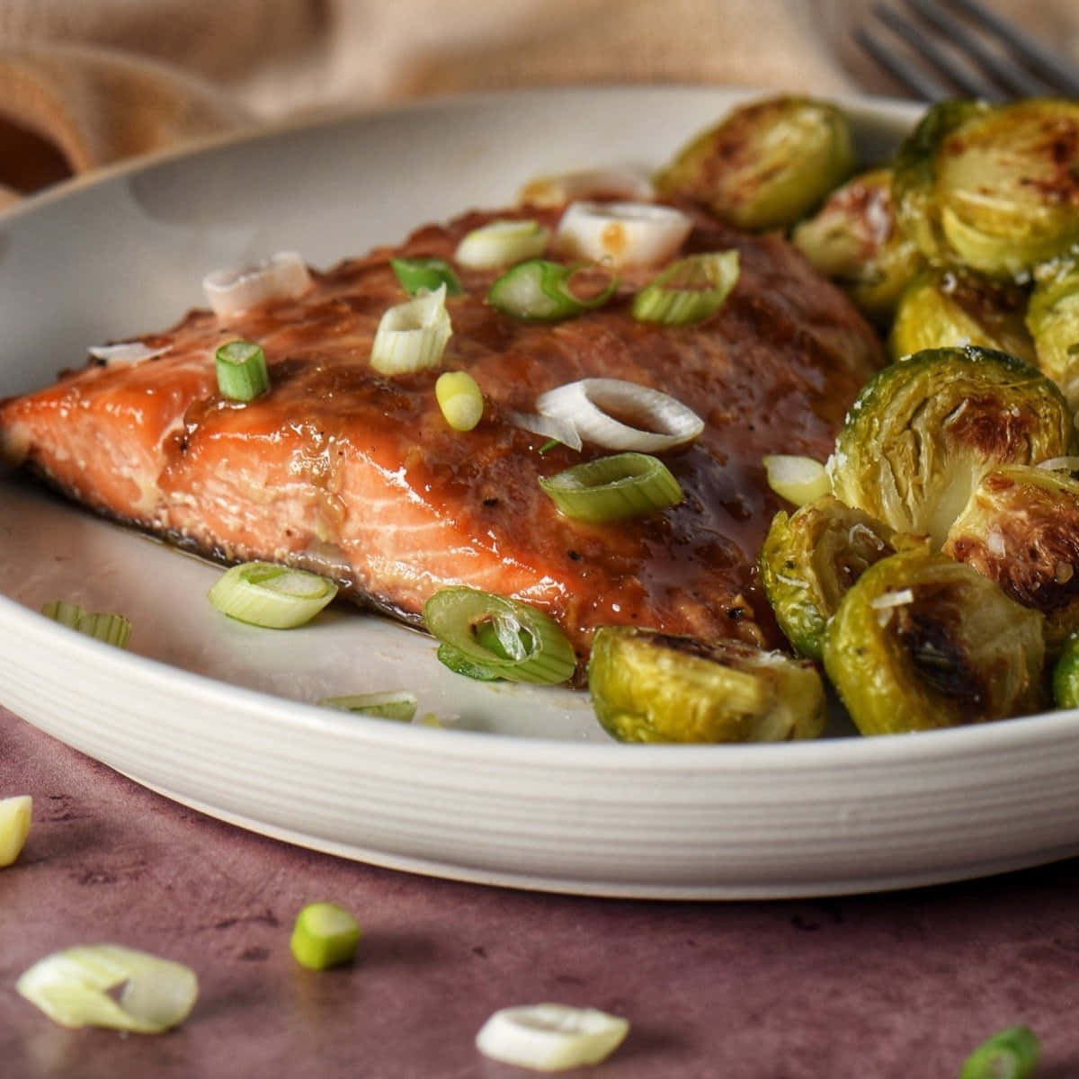 Salmon 桌布 壁紙 — 一塊光澤的釉面鮭魚排，上面放有切片青蔥，旁邊是烤孢子甘藍，放在白色盤子上。