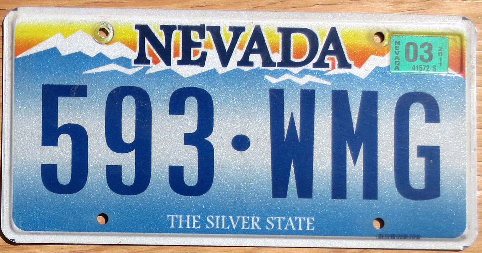 License Plate 桌布 壁紙 — 一塊內華達州車牌，帶有山脈和日落設計，放置在木質表面上。
