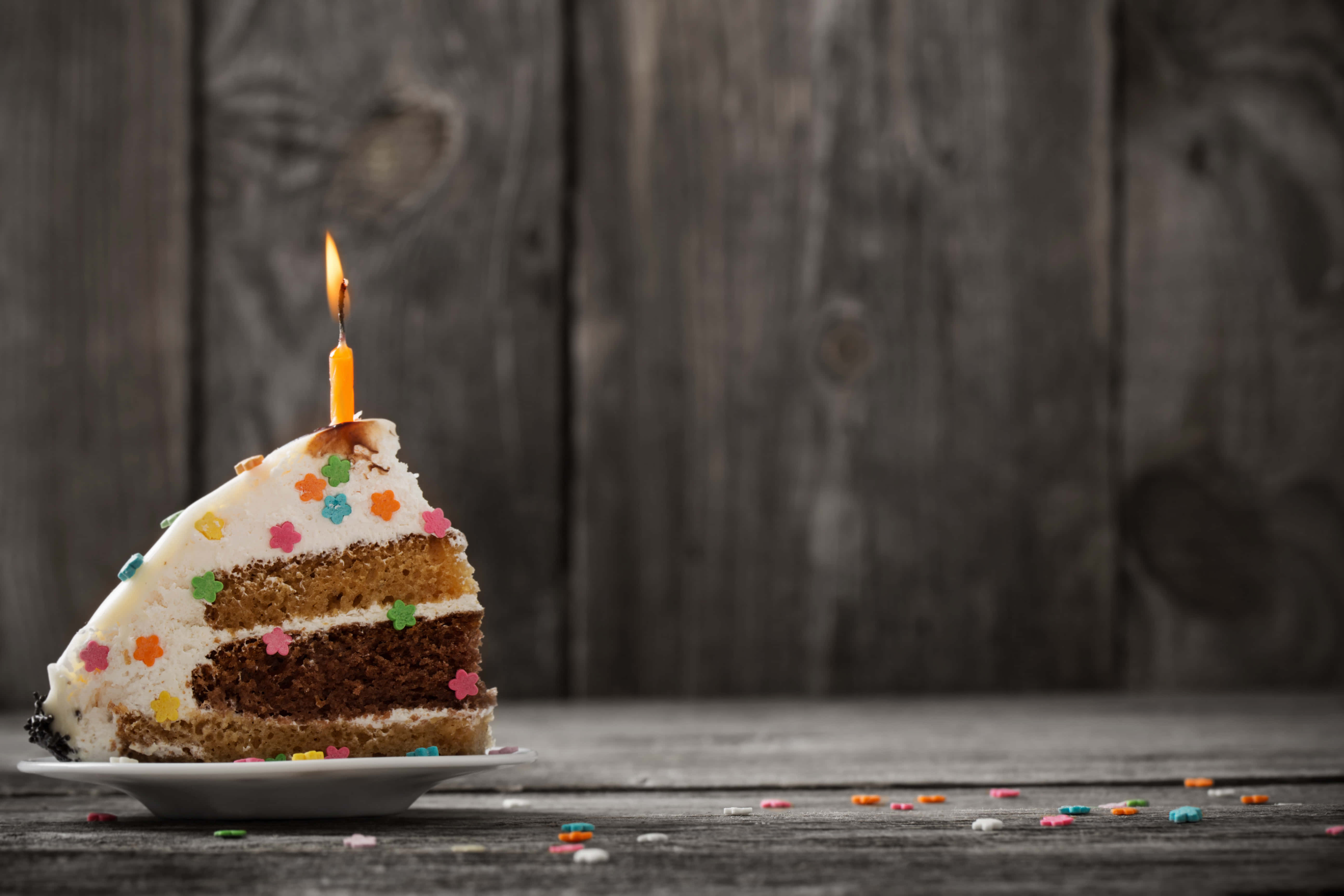 Birthday Cake 桌布 壁紙 — 一塊分層生日蛋糕，上面有燃燒的蠟燭和彩色糖粒，放在質樸的木桌上。