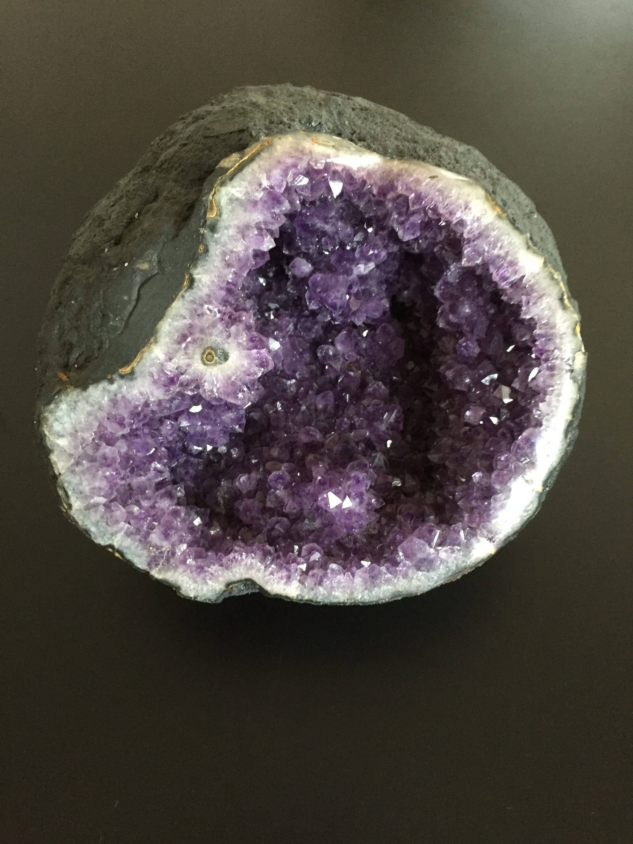 紫水晶 桌布 壁紙 — 一塊切割的紫水晶晶洞在黑色表面上展現出閃閃發光的紫色晶體，外部為深灰色。