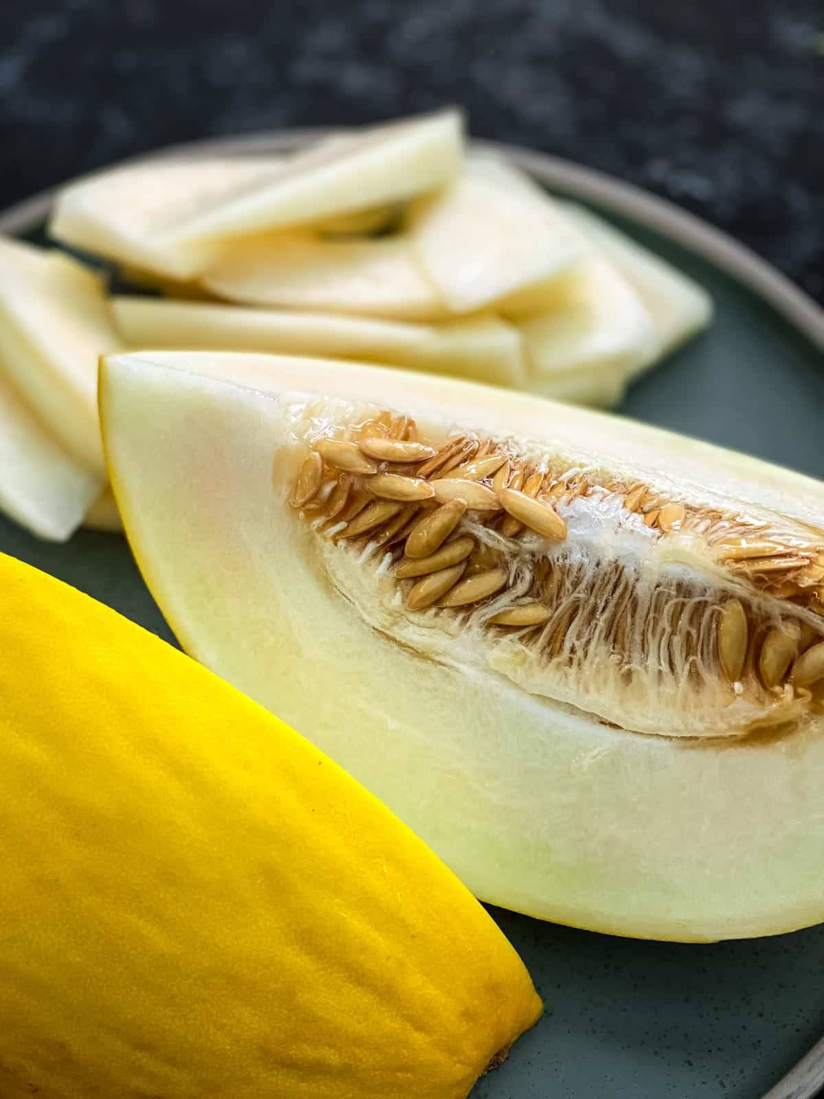 Fruit 桌布 壁紙 — 一塊切開的黃色哈密瓜，帶有種子和淡色果肉，放在一個深色盤子上，旁邊是一個完整的哈密瓜。