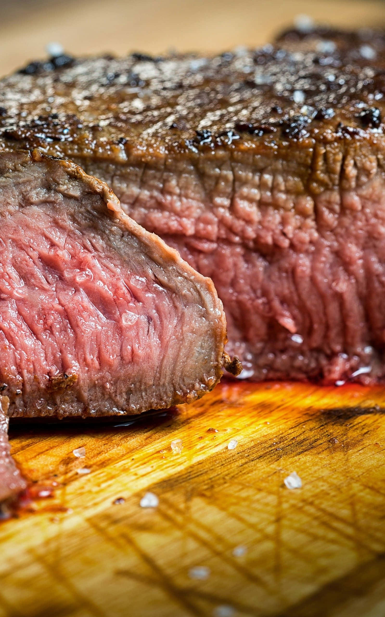 肉 桌布 壁紙 — 一塊多汁的 medium-rare 牛排，帶有焦脆外皮，放在灑滿粗鹽的木砧板上。