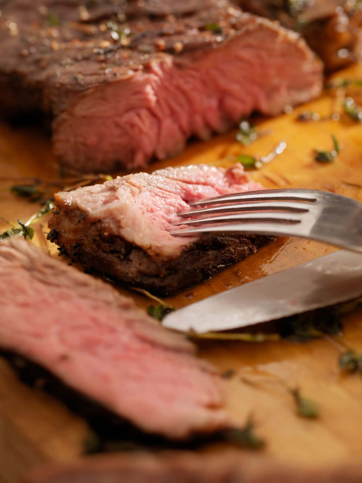 Red Meat 桌布 壁紙 — 一塊多汁的 medium-rare 牛排切片放在木板上，搭配新鮮香草，叉子擱在嫩肉片上。