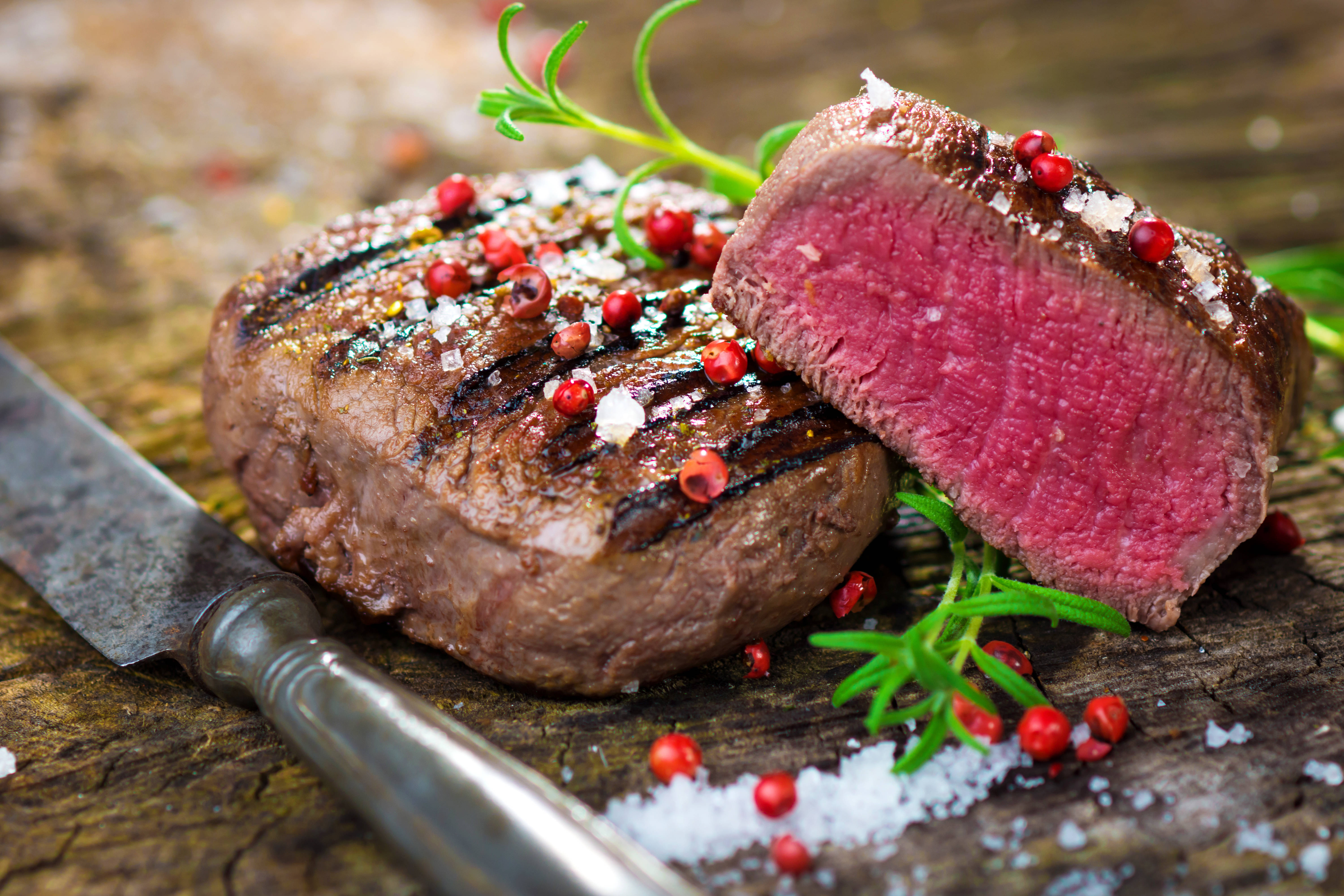 meat 桌布 壁紙 — 一塊多汁的 medium-rare 牛排帶有烤痕和胡椒粒，放在質樸的木板上，旁邊有一把刀。