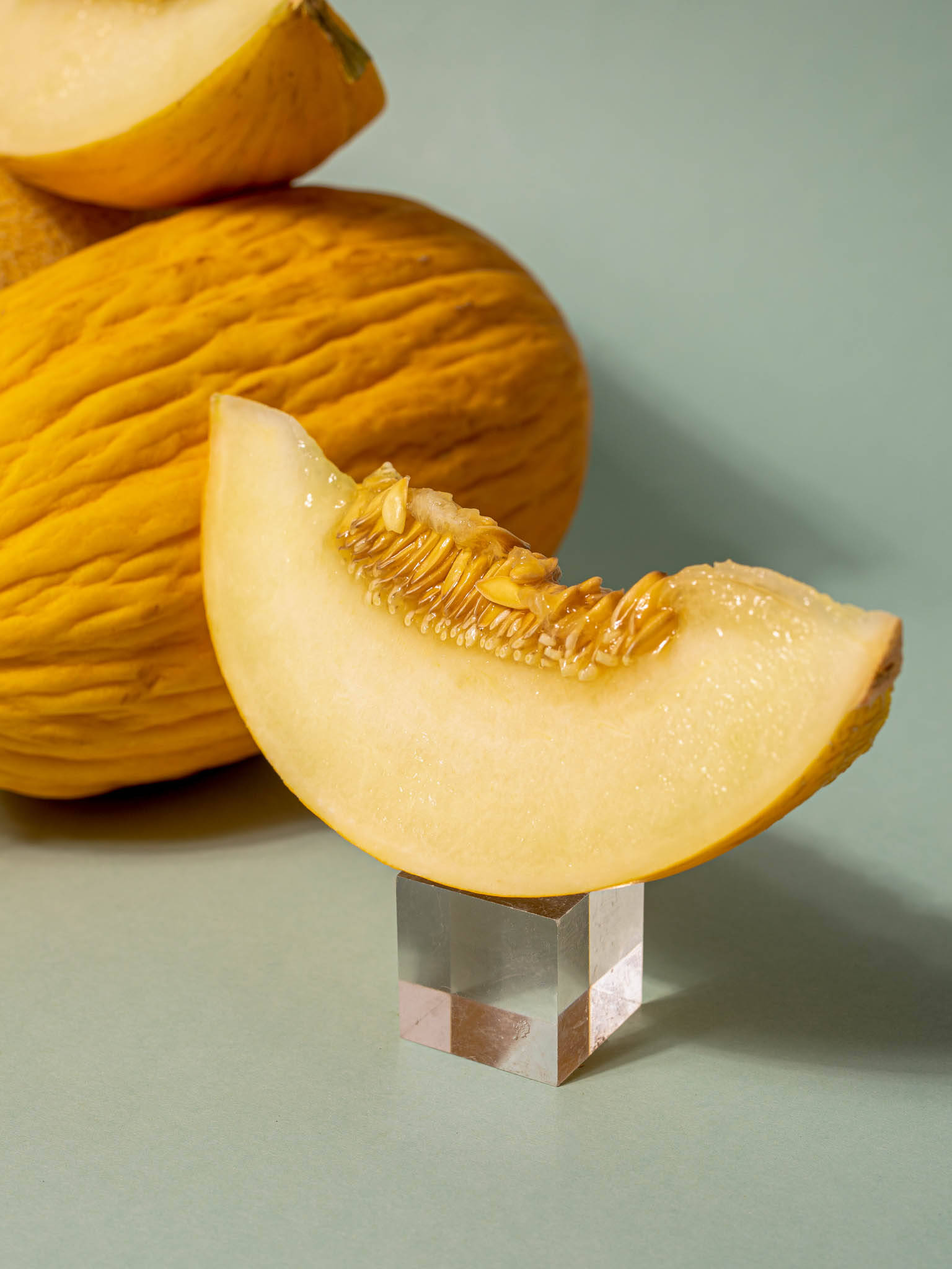 Fruit 桌布 壁紙 — 一塊多汁的哈密瓜片放在透明立方體底座上，旁邊是整個哈密瓜，背景是柔和的綠色。