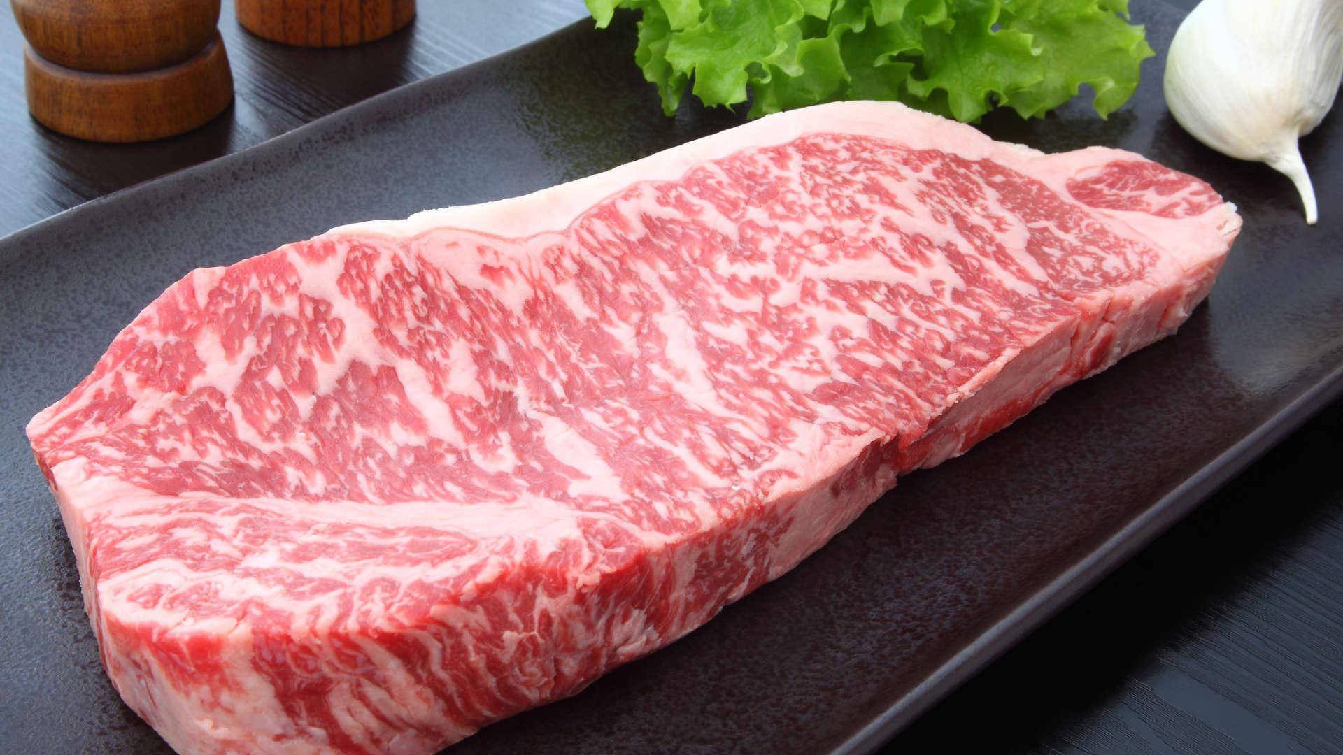 meat 桌布 壁紙 — 一塊多汁的大理石紋牛肉排放在深色盤子上，旁邊有新鮮生菜和大蒜。
