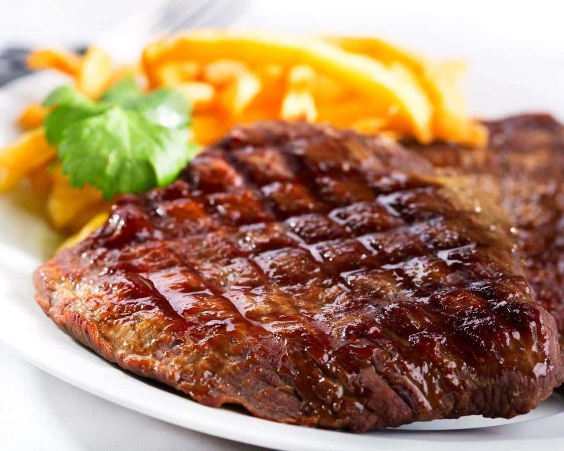 Steak 桌布 壁紙 — 一塊多汁的烤牛排帶有明顯的烤痕，旁邊放著金黃色的薯條和新鮮的香菜葉，盛在白色盤子上。