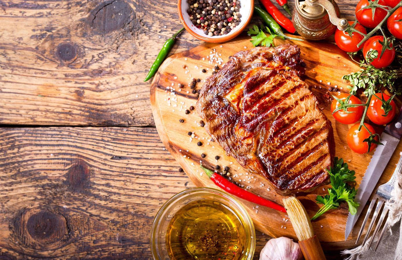 meat 桌布 壁紙 — 一塊多汁的烤牛排帶有烤痕，放在木板上，周圍環繞著櫻桃番茄、新鮮香草和香料。