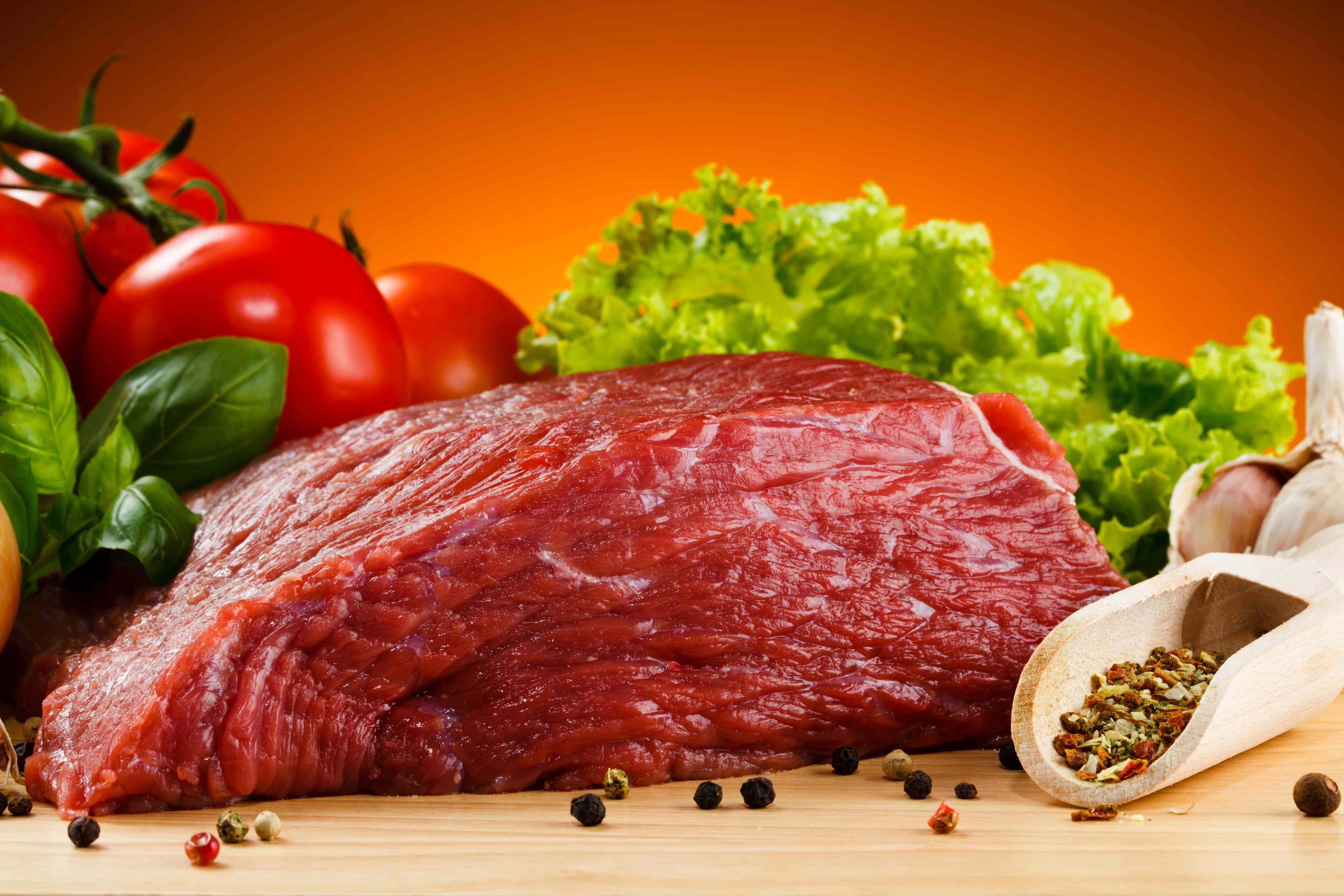 meat 桌布 壁紙 — 一塊多汁的生牛肉排放在木板上，周圍是新鮮的番茄、羅勒、生菜、大蒜和胡椒粒，背景是溫暖的橙色。