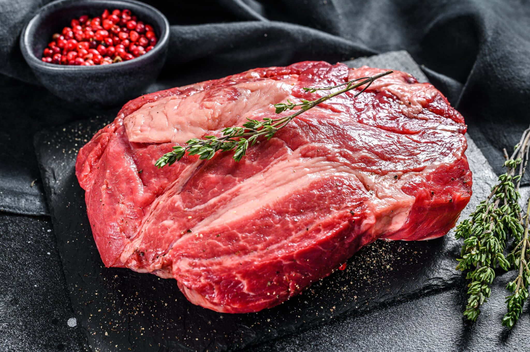 Red Meat 桌布 壁紙 — 一塊多汁的生牛肉排放在深色石板板上，飾以新鮮百里香和紅胡椒粒。