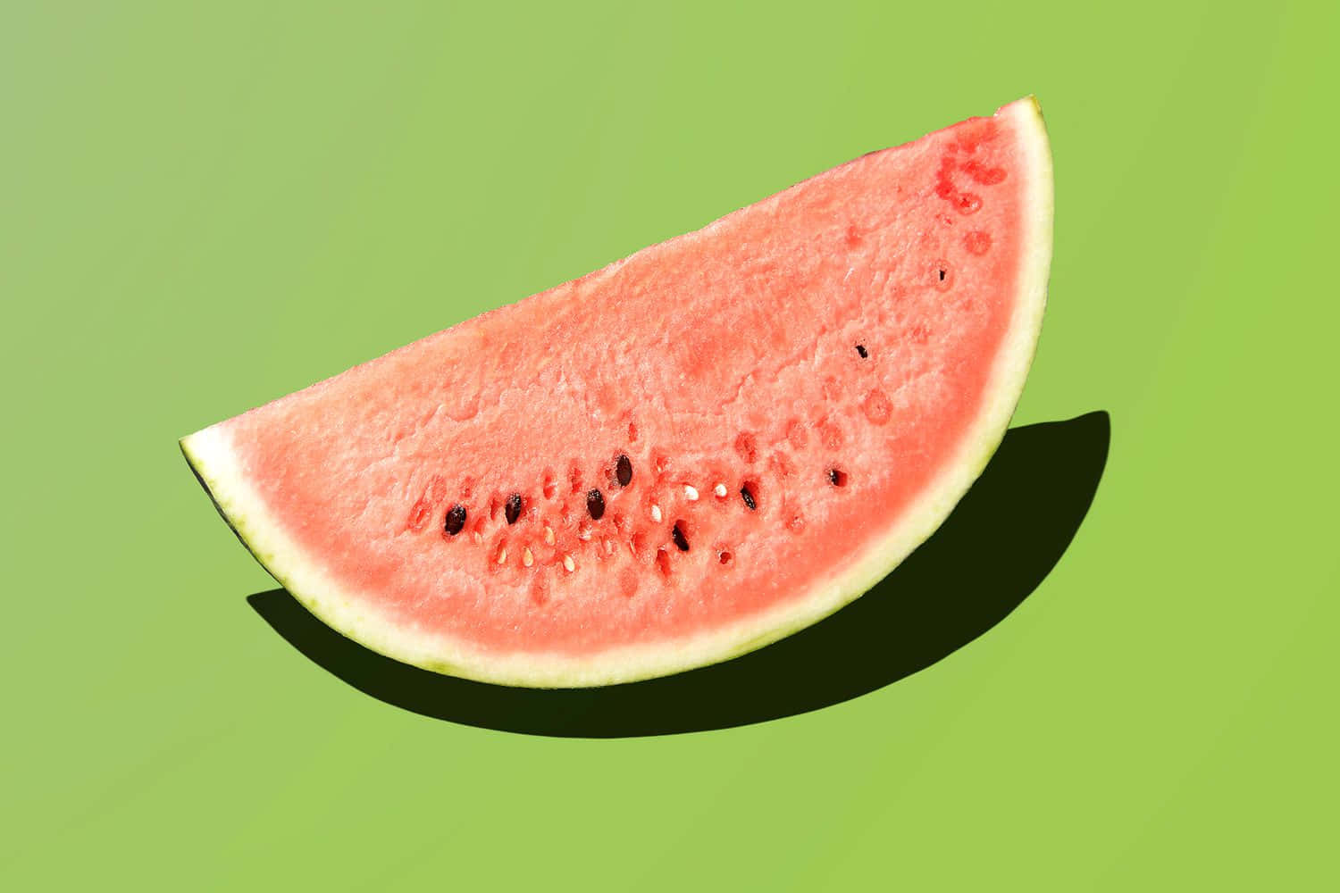 Fruit 桌布 壁紙 — 一塊多汁的西瓜片，帶有黑色種子，放在充滿活力的綠色背景上，投下大膽的陰影。