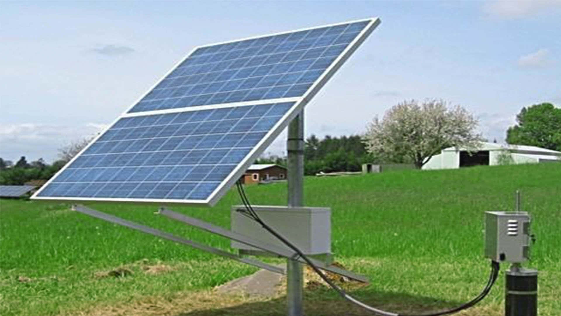 Solar 桌布 壁紙 — 一塊大型藍色太陽能板傾斜地立在翠綠的田野中，天空部分多雲，遠處有樹木和穀倉。