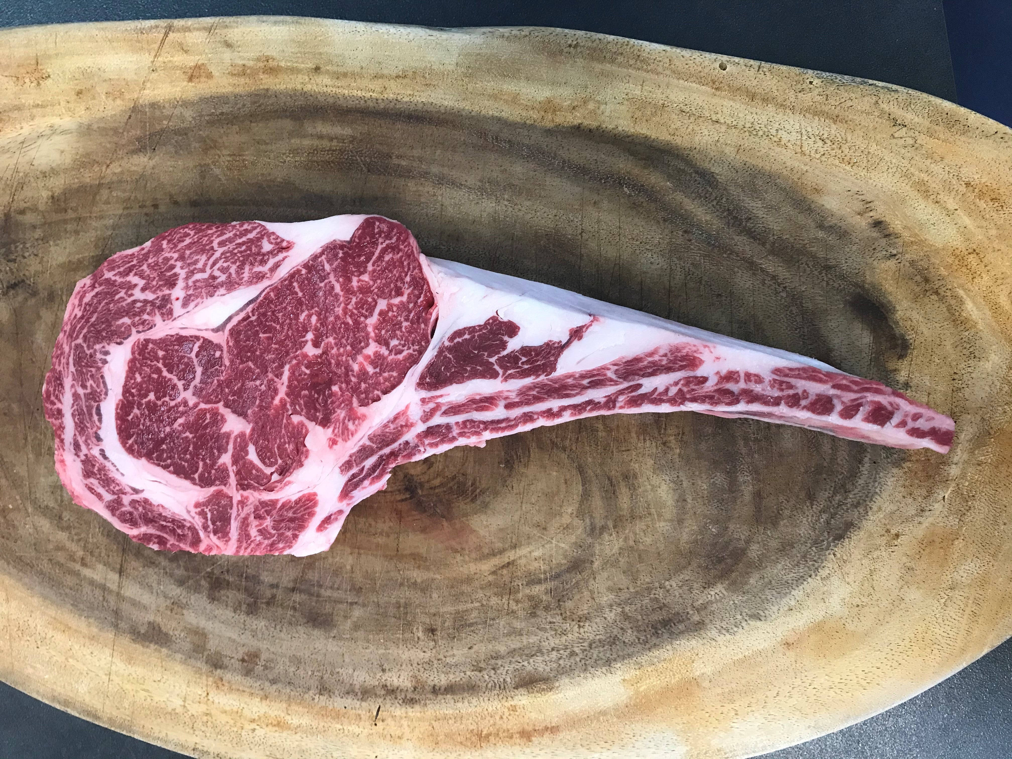 meat 桌布 壁紙 — 一塊完美大理石紋的戰斧牛排放在質樸的木砧板上，木紋豐富。