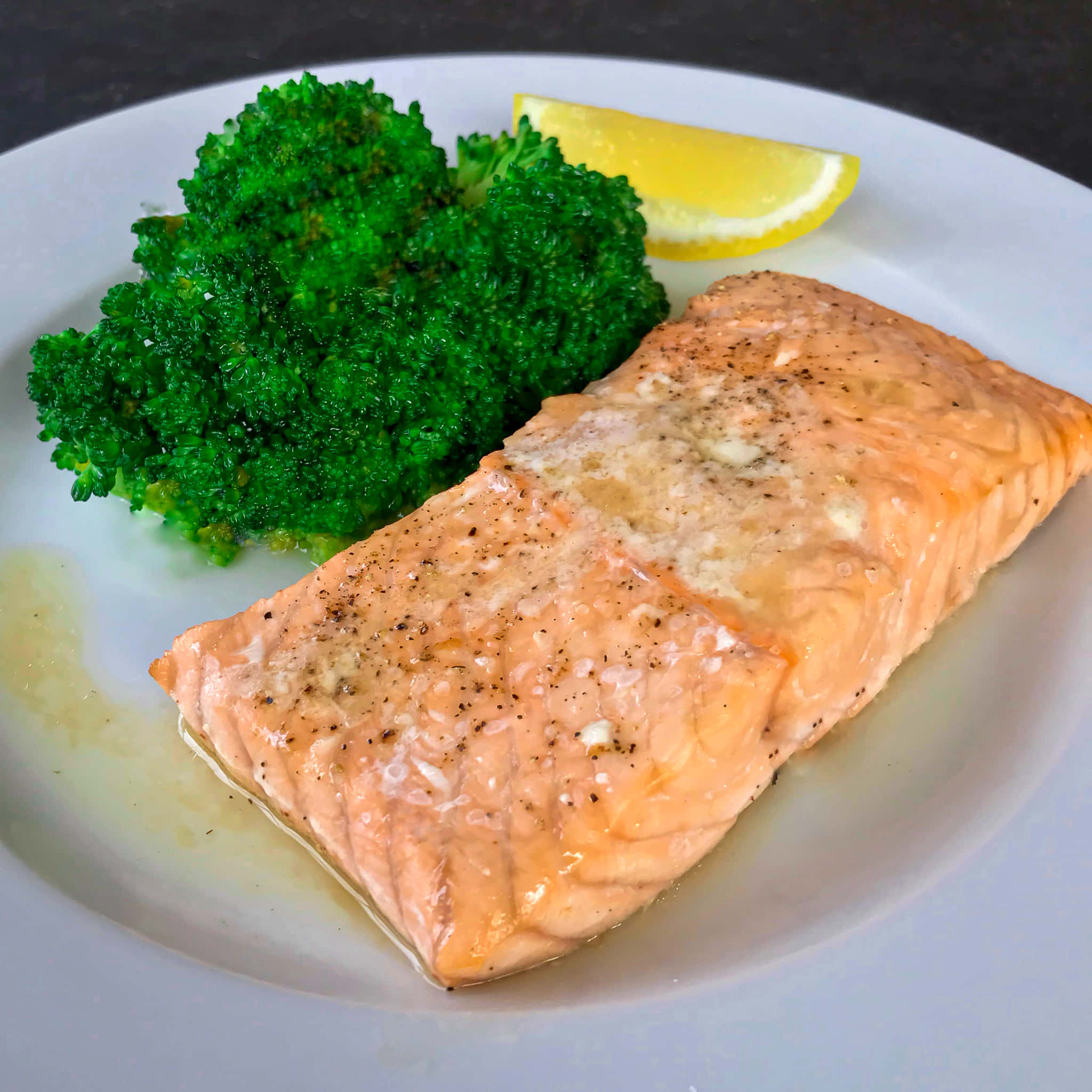 Salmon 桌布 壁紙 — 一塊完美烹調的鮭魚菲力，配上奶油和胡椒，旁邊放著鮮綠的花椰菜和檸檬角，置於白色盤子上。