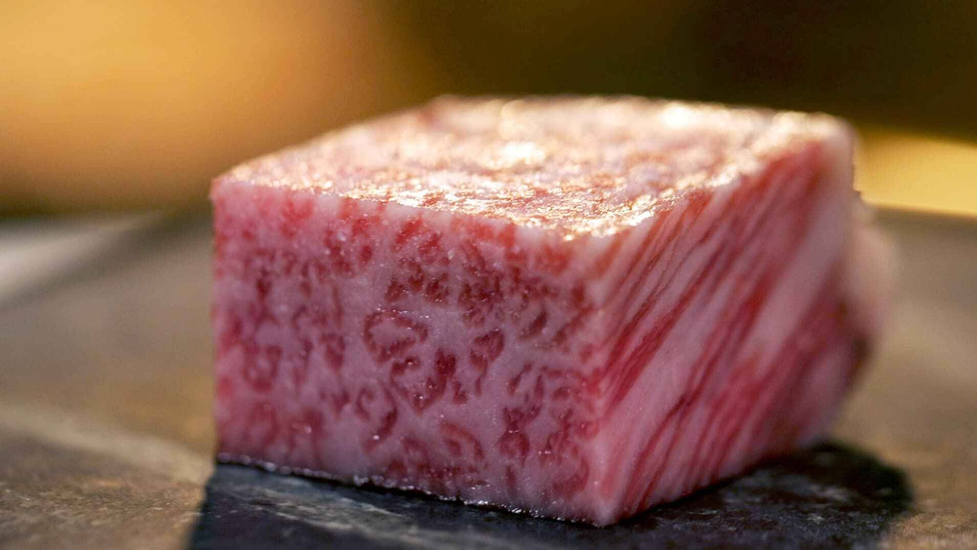 meat 桌布 壁紙 — 一塊完美煎封的和牛方塊，雪花脂肪在深色石板盤上溫暖燈光下閃閃發光。