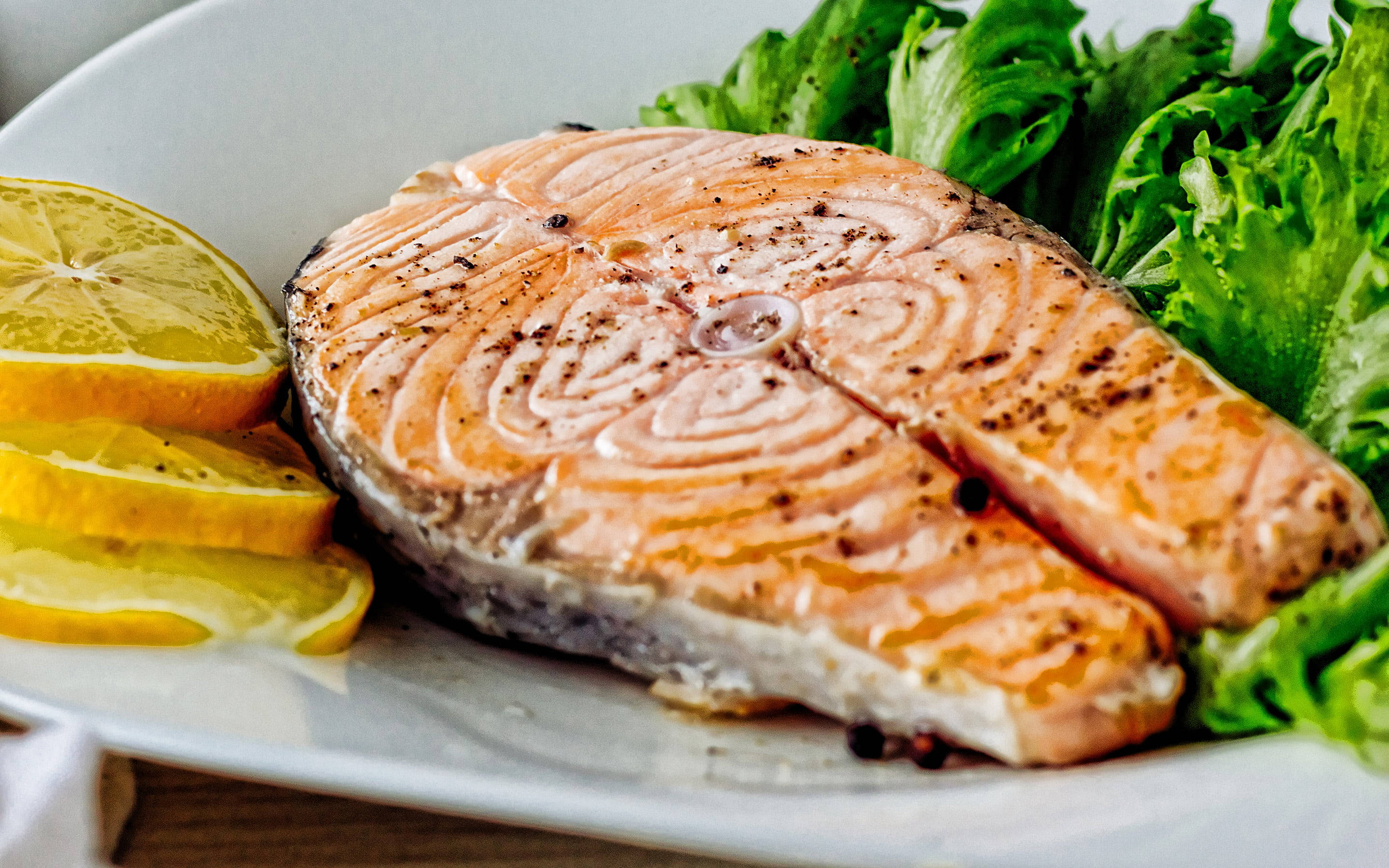 Delicious Food 桌布 壁紙 — 一塊完美煎封的黑椒鮭魚片放在綠色生菜床上，旁邊有檸檬片，置於白色盤子上。