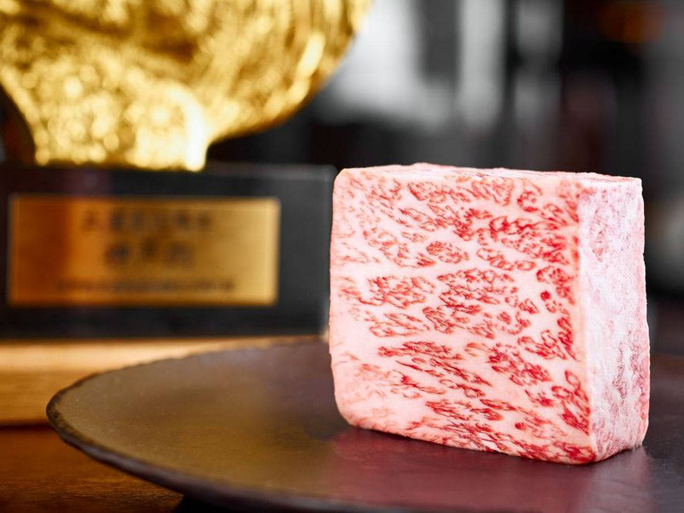 meat 桌布 壁紙 — 一塊完美的大理石紋和牛立方體放在深色盤子上，旁邊有一個閃閃發光的金色獎盃。