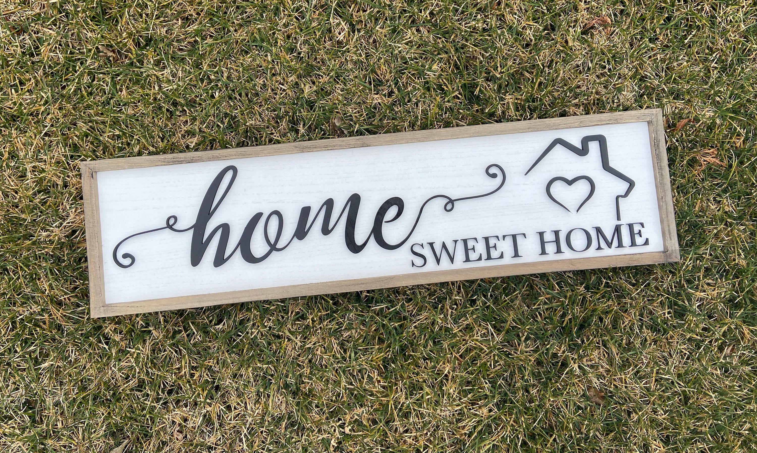 Home Sweet Home 桌布 壁紙 — 一塊寫有「home sweet home」的質樸木牌，帶有心形房屋圖標，放置在綠色和棕色的草地上。