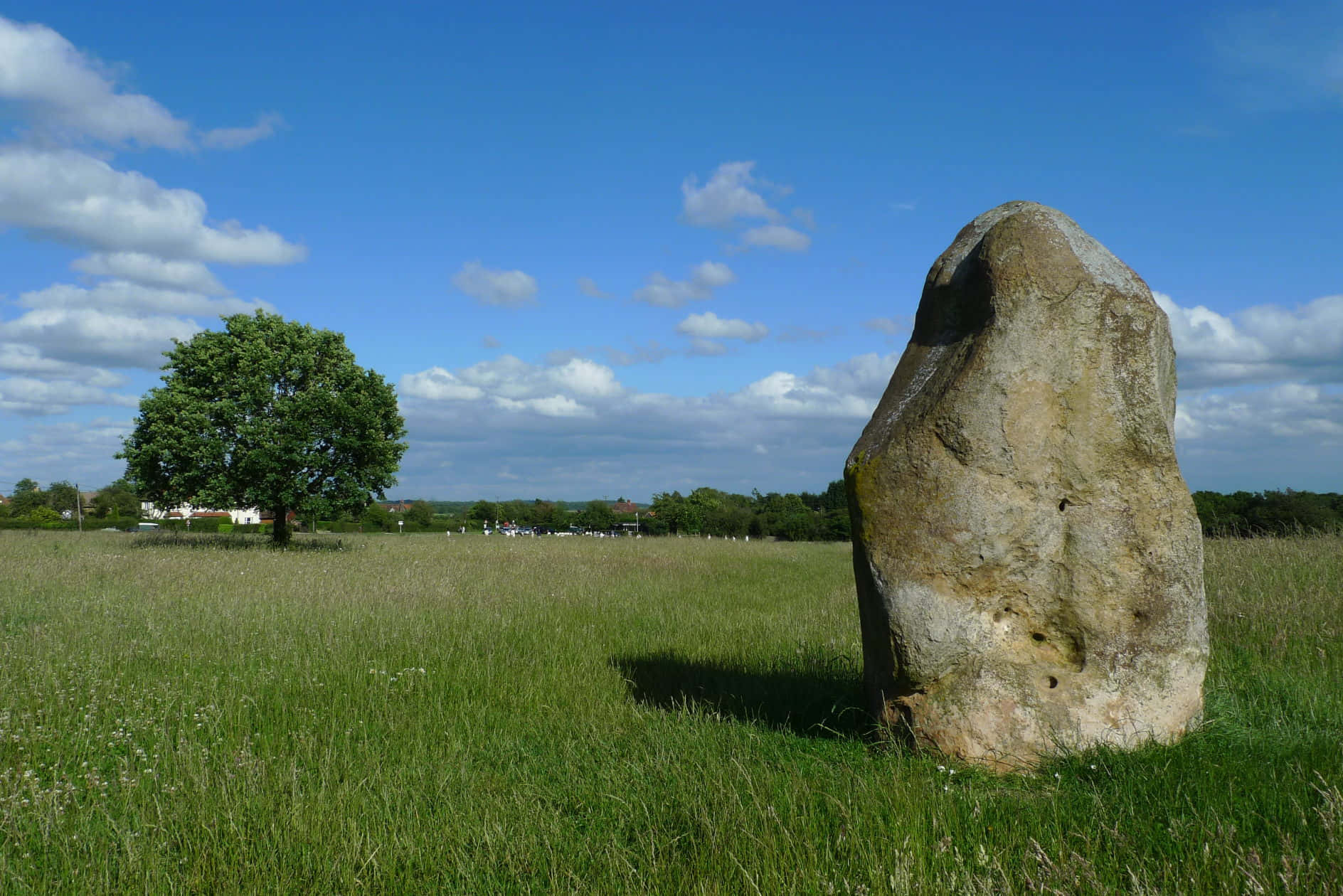 Stone 桌布 壁紙 — 一塊巨大的古代立石從陽光明媚的綠色田野中升起，天空湛藍，點綴著蓬鬆的白雲。