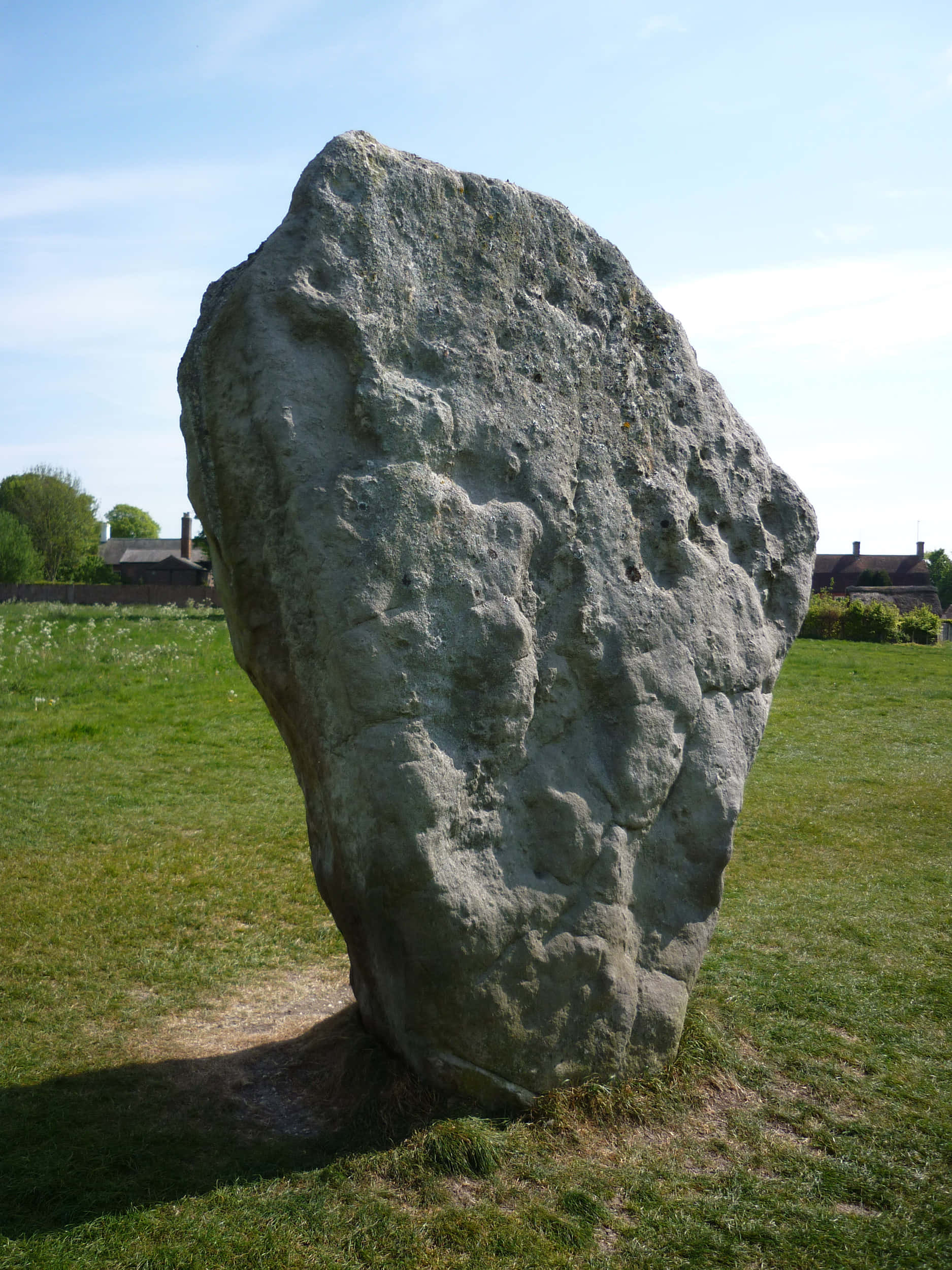 Stone 桌布 壁紙 — 一塊巨大的古代豎立石頭從陽光照耀的綠色田野中升起，在清澈的藍天下，遠處可見房屋。