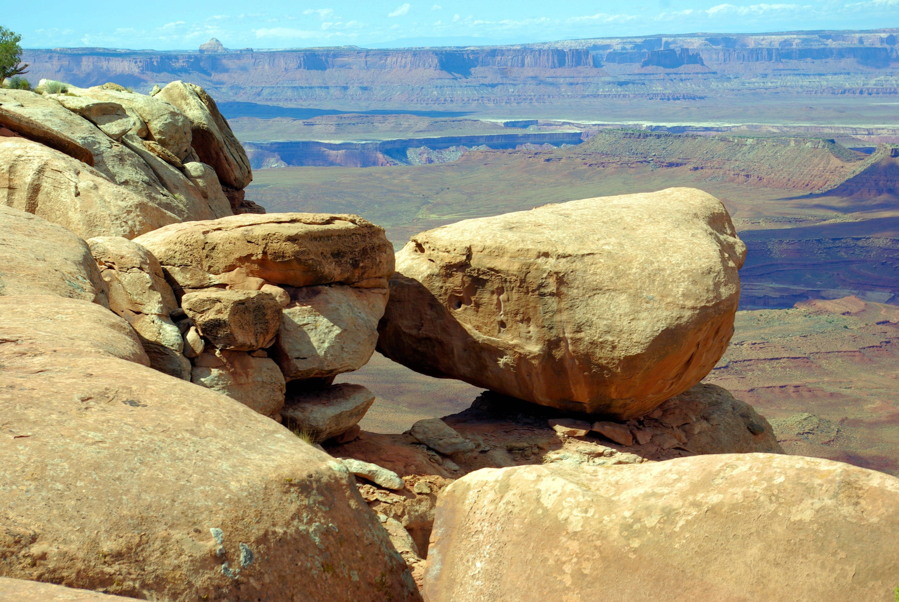 Canyonlands National Park 桌布 壁紙 — 一塊巨大的平衡石頭不穩定地棲息在岩石露頭上，俯瞰著廣闊的沙漠峽谷，天空清澈湛藍。