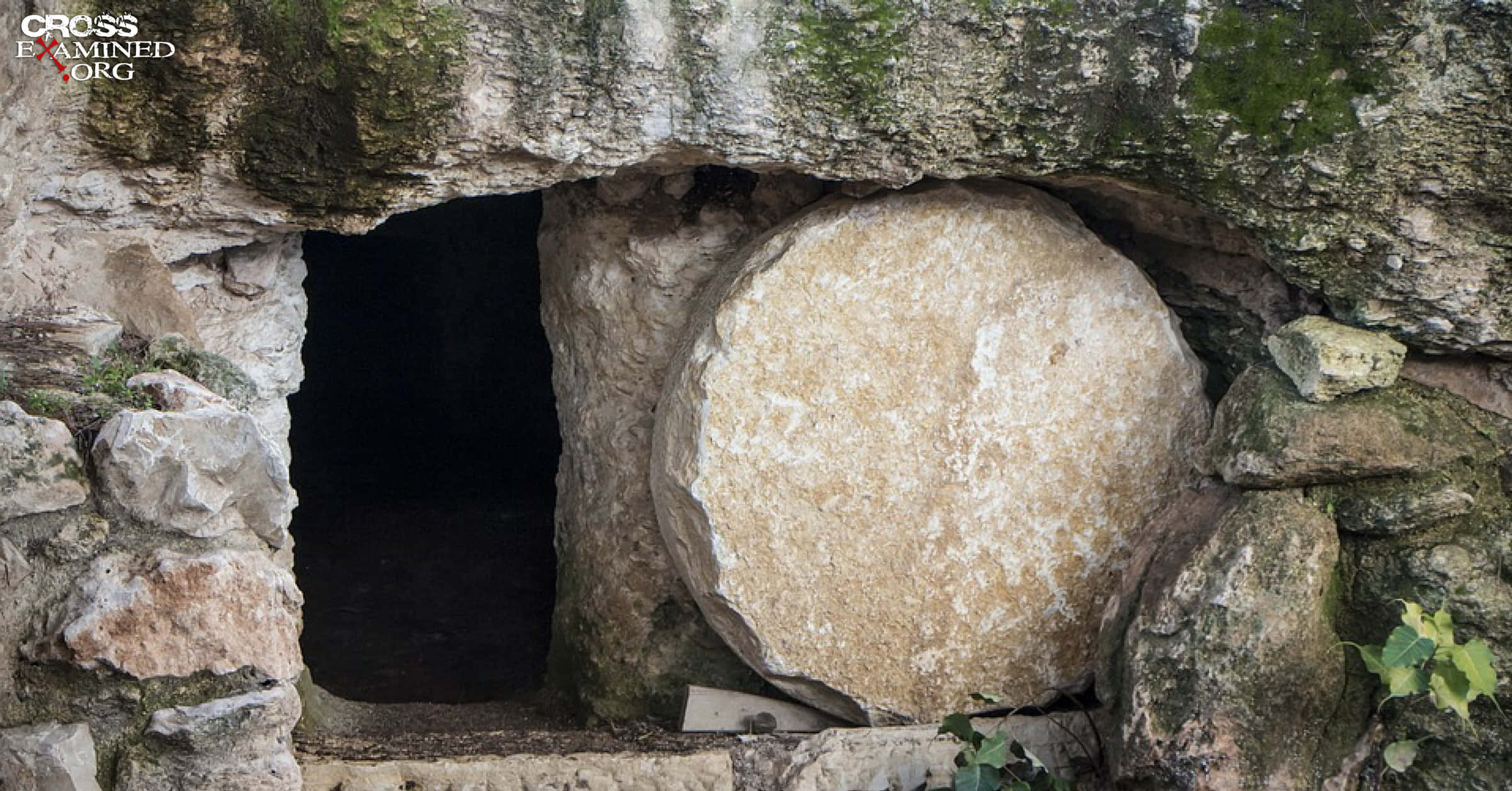 Empty Tomb 桌布 壁紙 — 一塊巨大的石板封住了古老岩石墓穴的入口，周圍有長滿苔蘚的石頭和黑暗的內部。