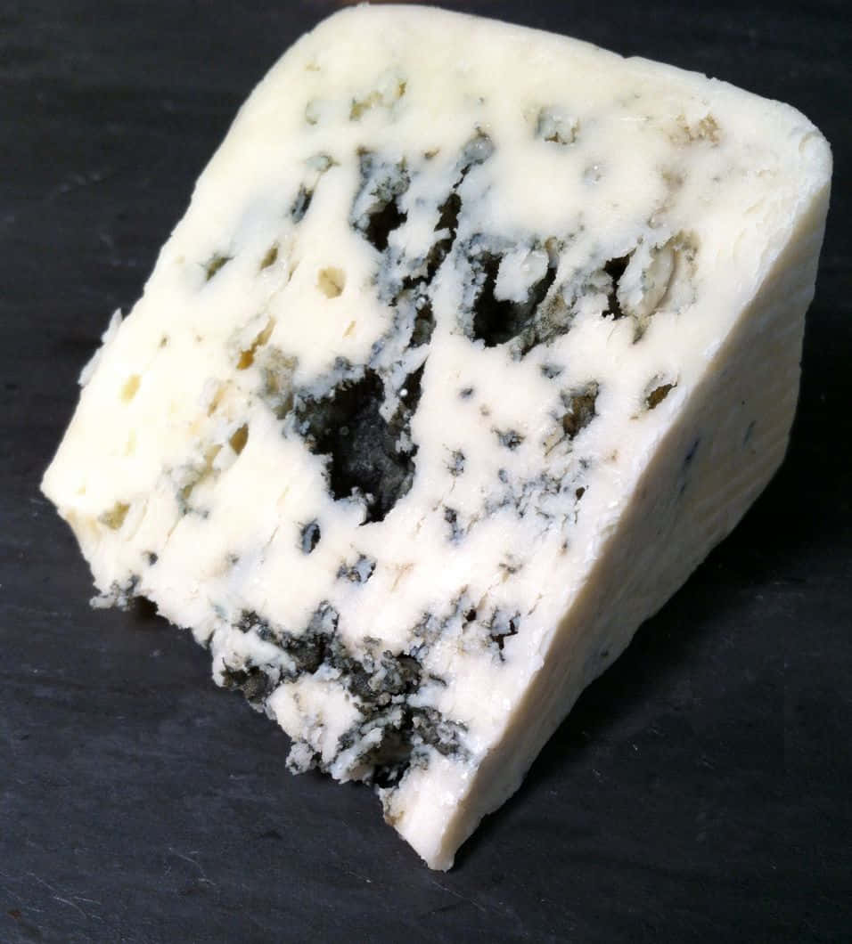 Blue Cheese 桌布 壁紙 — 一塊帶有大理石紋藍色脈絡的奶油藍紋起司，放在深色石板表面上。