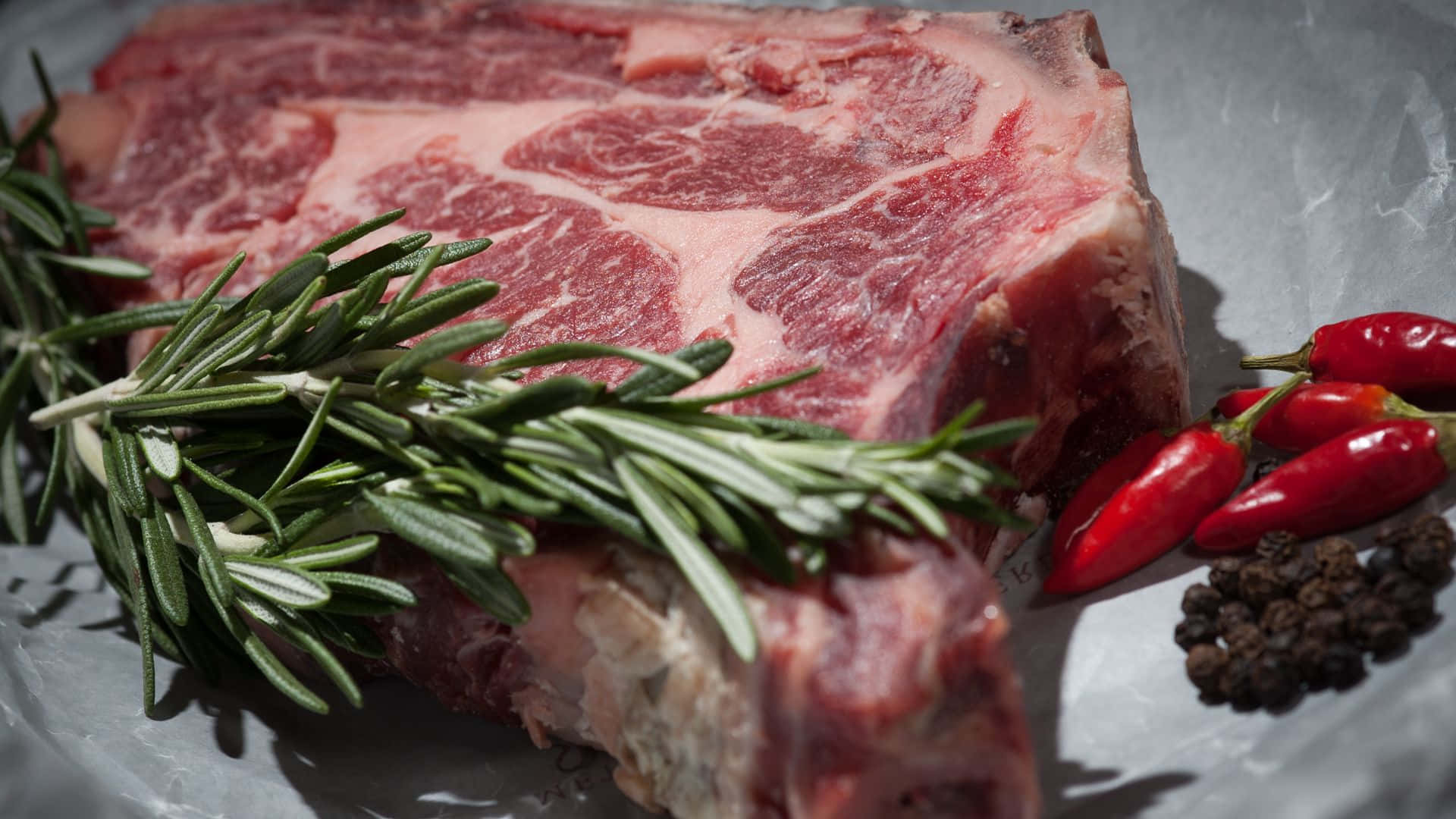 Red Meat 桌布 壁紙 — 一塊帶有大理石花紋的生牛肉排放在鋁箔紙上，旁邊有迷迭香、紅辣椒和胡椒粒。