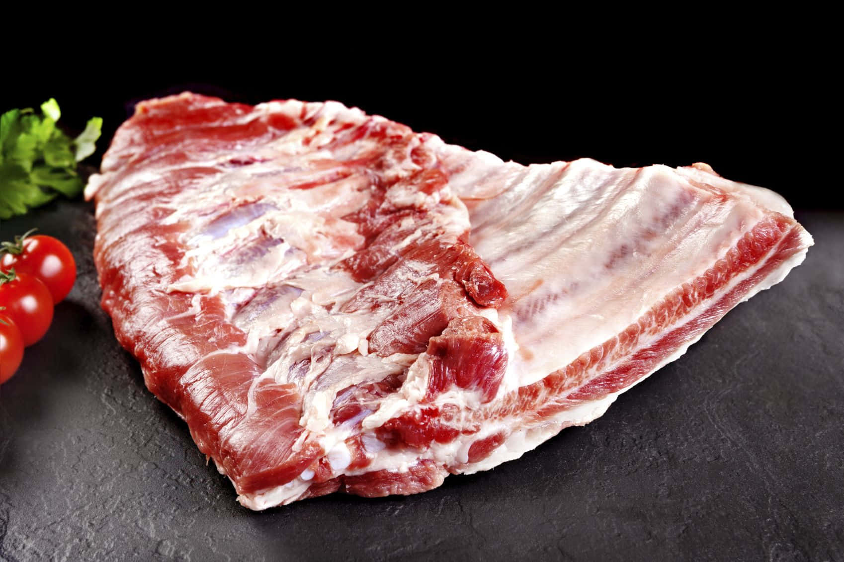 meat 桌布 壁紙 — 一塊帶有大理石花紋的生牛肉肋眼牛排放在深色石板表面上，旁邊是新鮮的櫻桃番茄和荷蘭芹。