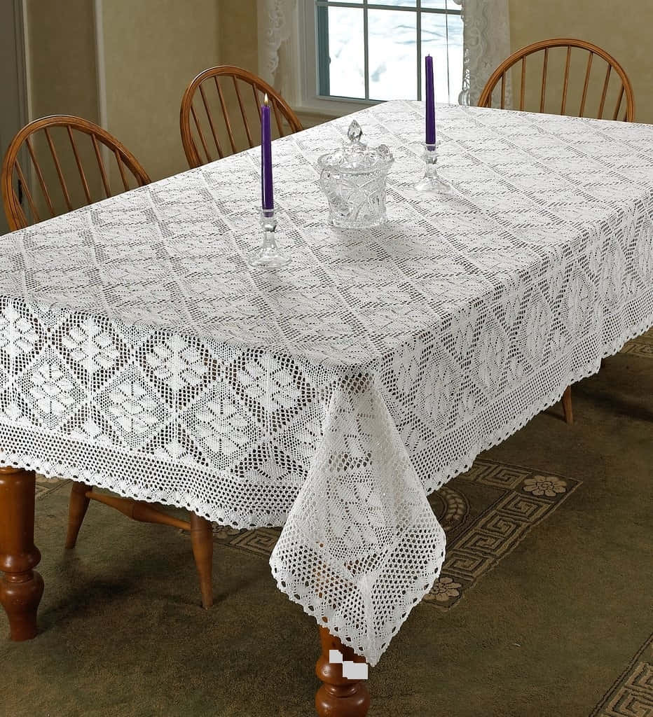 Crocheting 桌布 壁紙 — 一塊帶有幾何圖案的白色蕾絲桌布鋪在木製餐桌上，桌上擺有紫色蠟燭和一個玻璃罐。