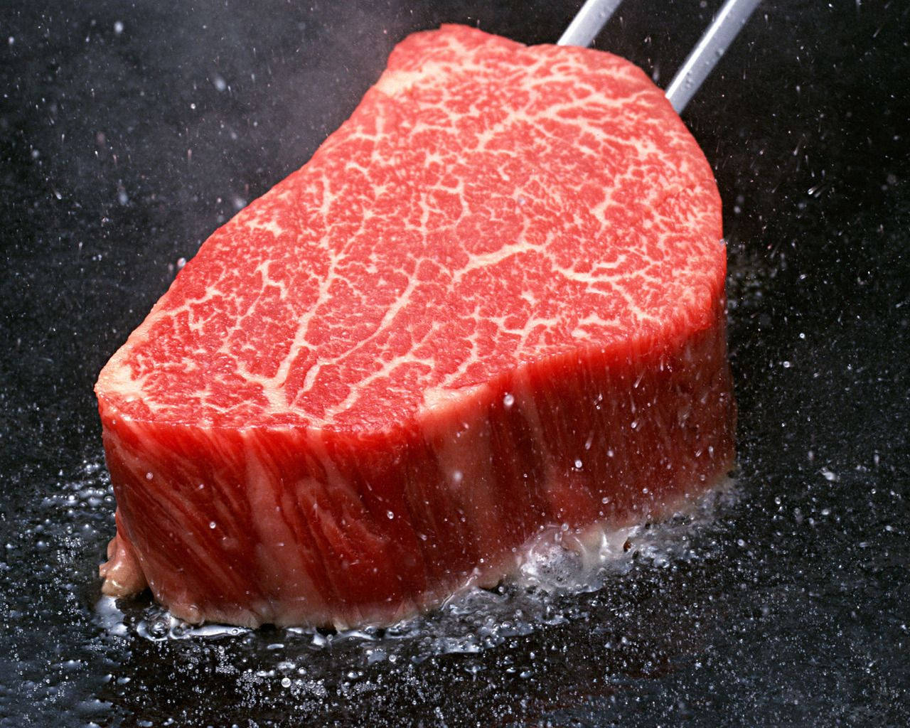meat 桌布 壁紙 — 一塊帶有油花的多汁生牛肉排在高溫黑鍋中滋滋作響，蒸氣裊裊升起。