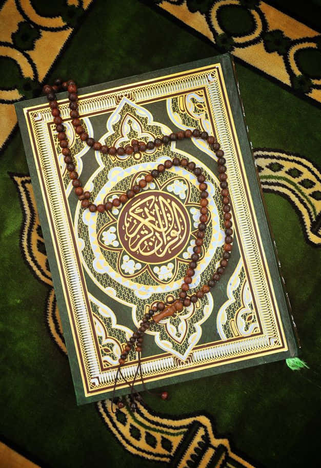 Quran 桌布 壁紙 — 一塊帶有複雜綠色和金色圖案的祈禱地毯，在寧靜的宗教環境中放著一本古蘭經和木製玫瑰經念珠。