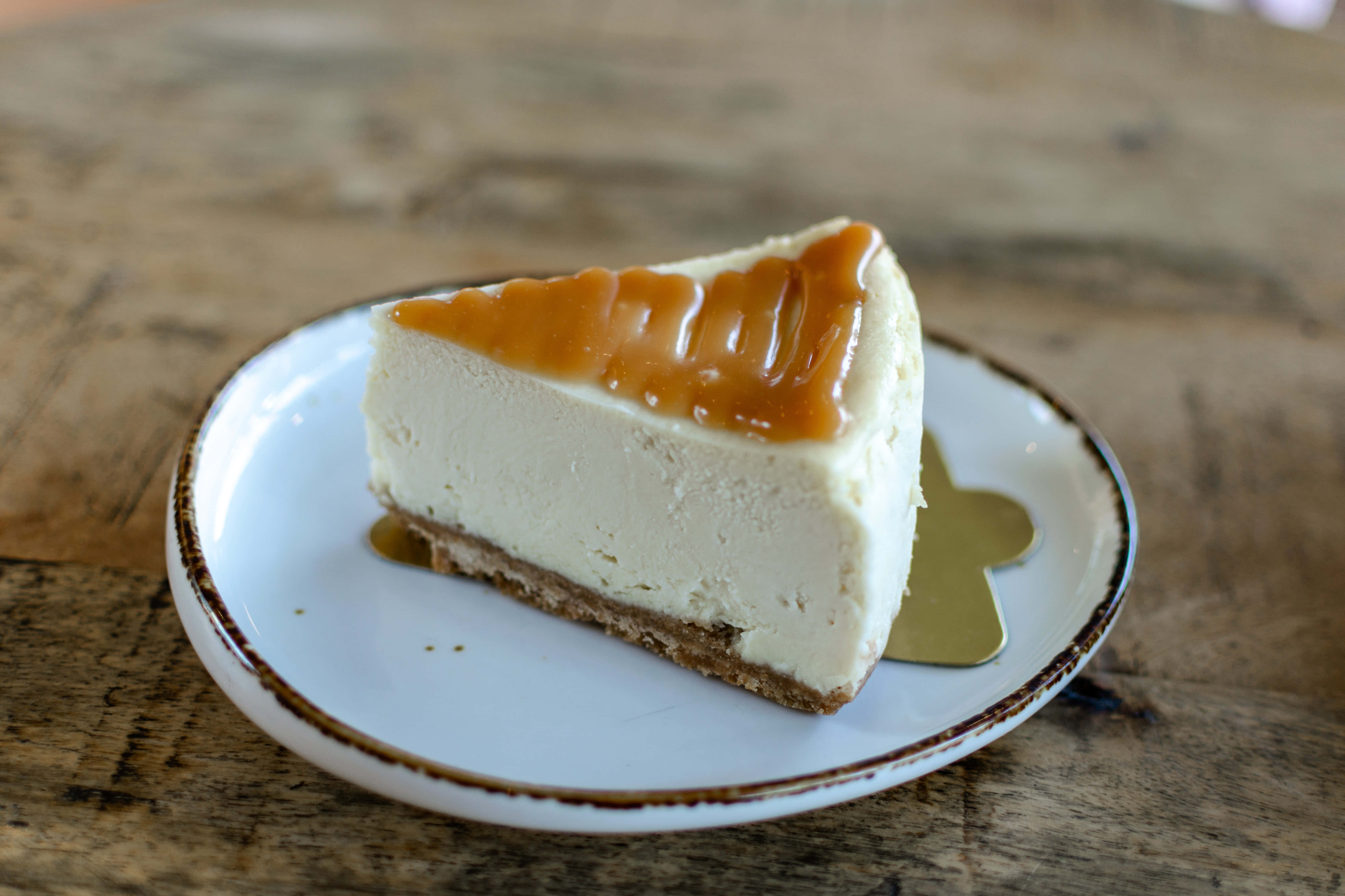 Caramel 桌布 壁紙 — 一塊幼滑的焦糖起司蛋糕放在一個有棕色邊的白色盤子上，擺在一張鄉村風格的木桌上。