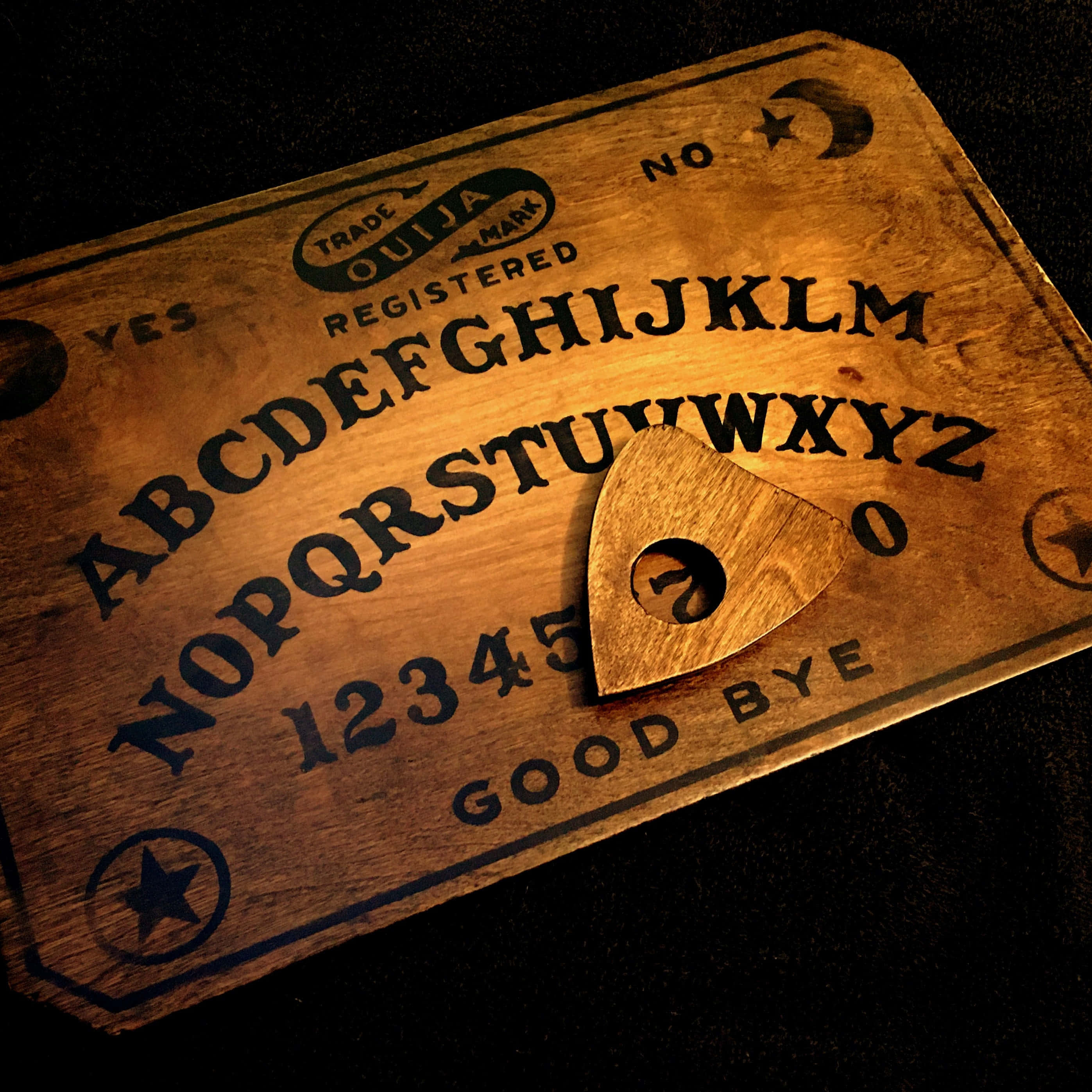 ouija board 桌布 壁紙 — 一塊復古木製通靈板連指示器，在溫暖燈光下置於深色背景上。