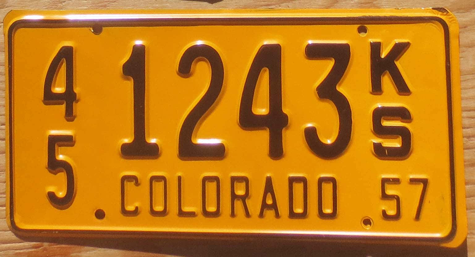License Plate 桌布 壁紙 — 一塊復古黃色科羅拉多州車牌，帶有黑色數字和字母，放置在木質表面上。