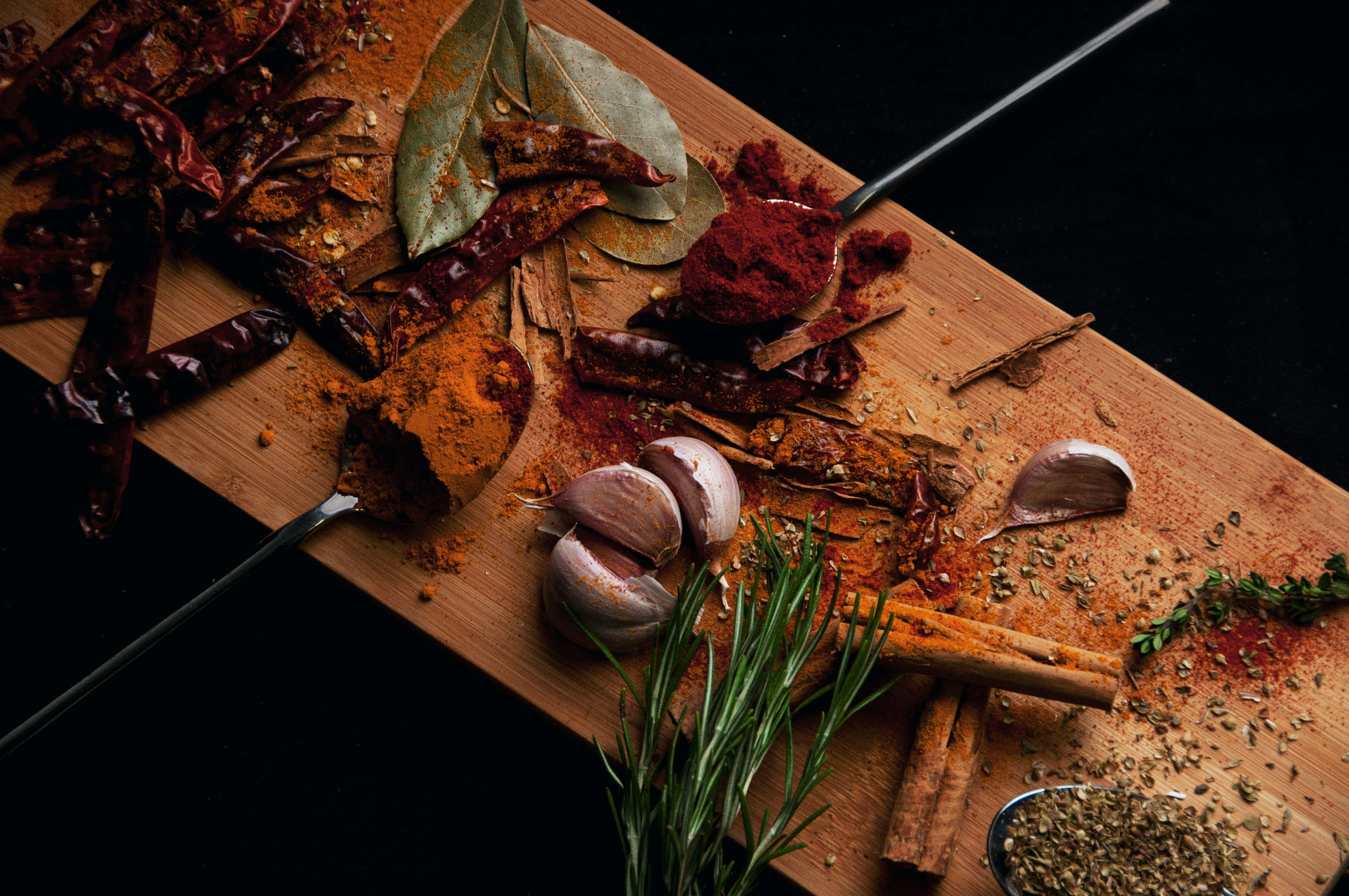 Spices 桌布 壁紙 — 一塊木板上展示著色彩鮮豔的香料，如辣椒粉、肉桂和迷迭香，背景為深色。
