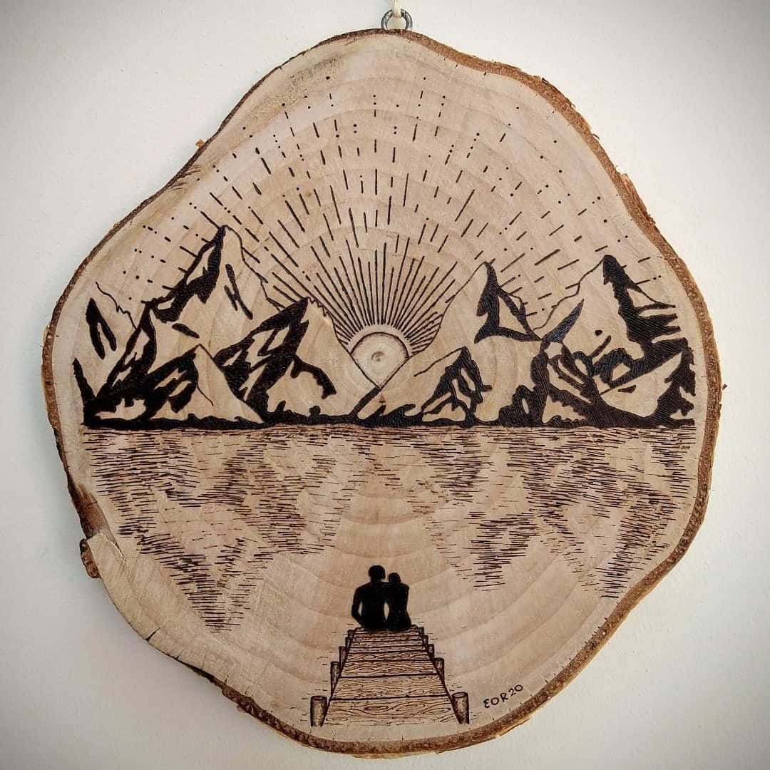 Wood Burning 桌布 壁紙 — 一塊木片上燒製的藝術品描繪了一對情侶在碼頭上凝視著平靜水面倒映的雪山背後的日出。