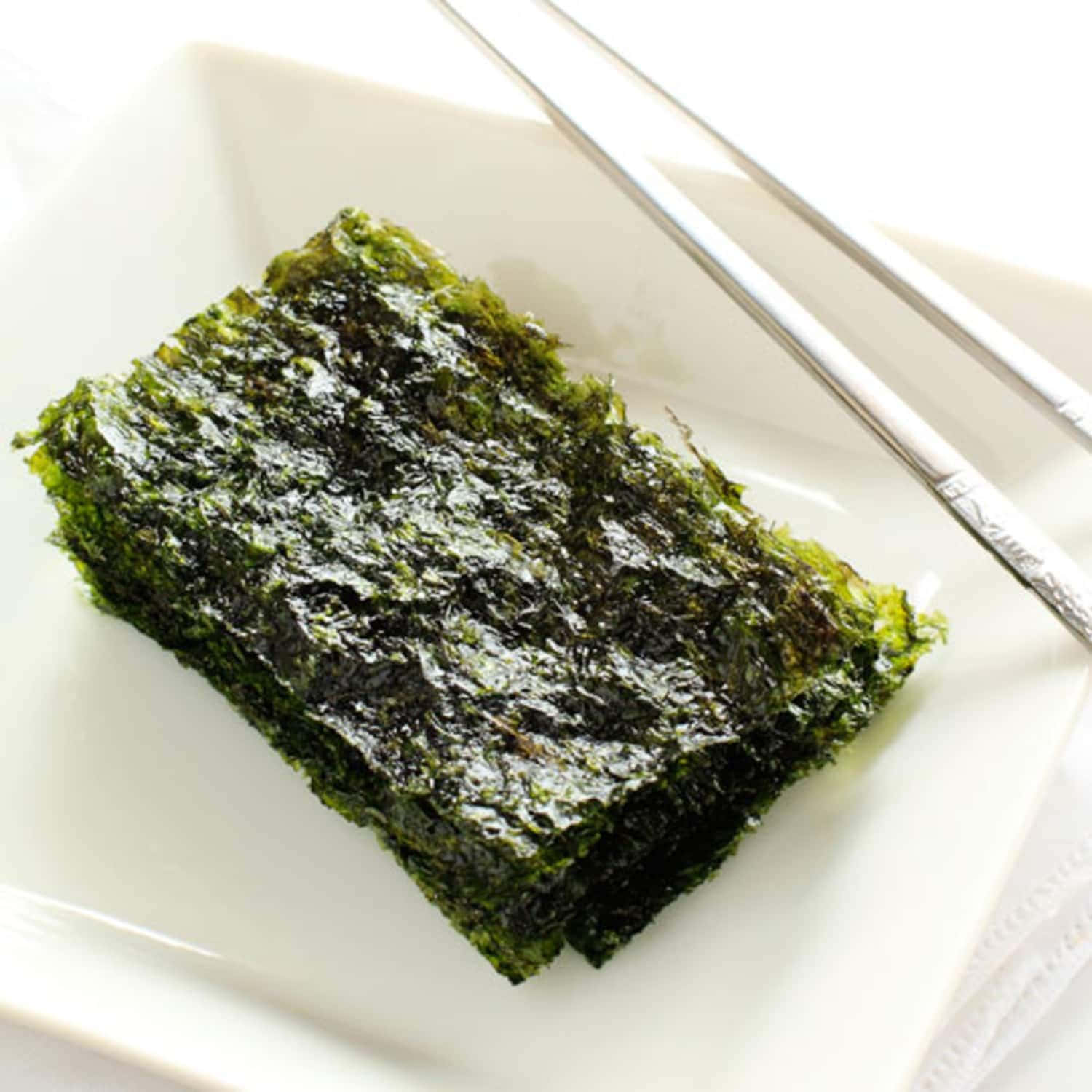 Seaweed 桌布 壁紙 — 一塊深綠色烤海苔放在白色盤子上，旁邊放著銀色筷子。