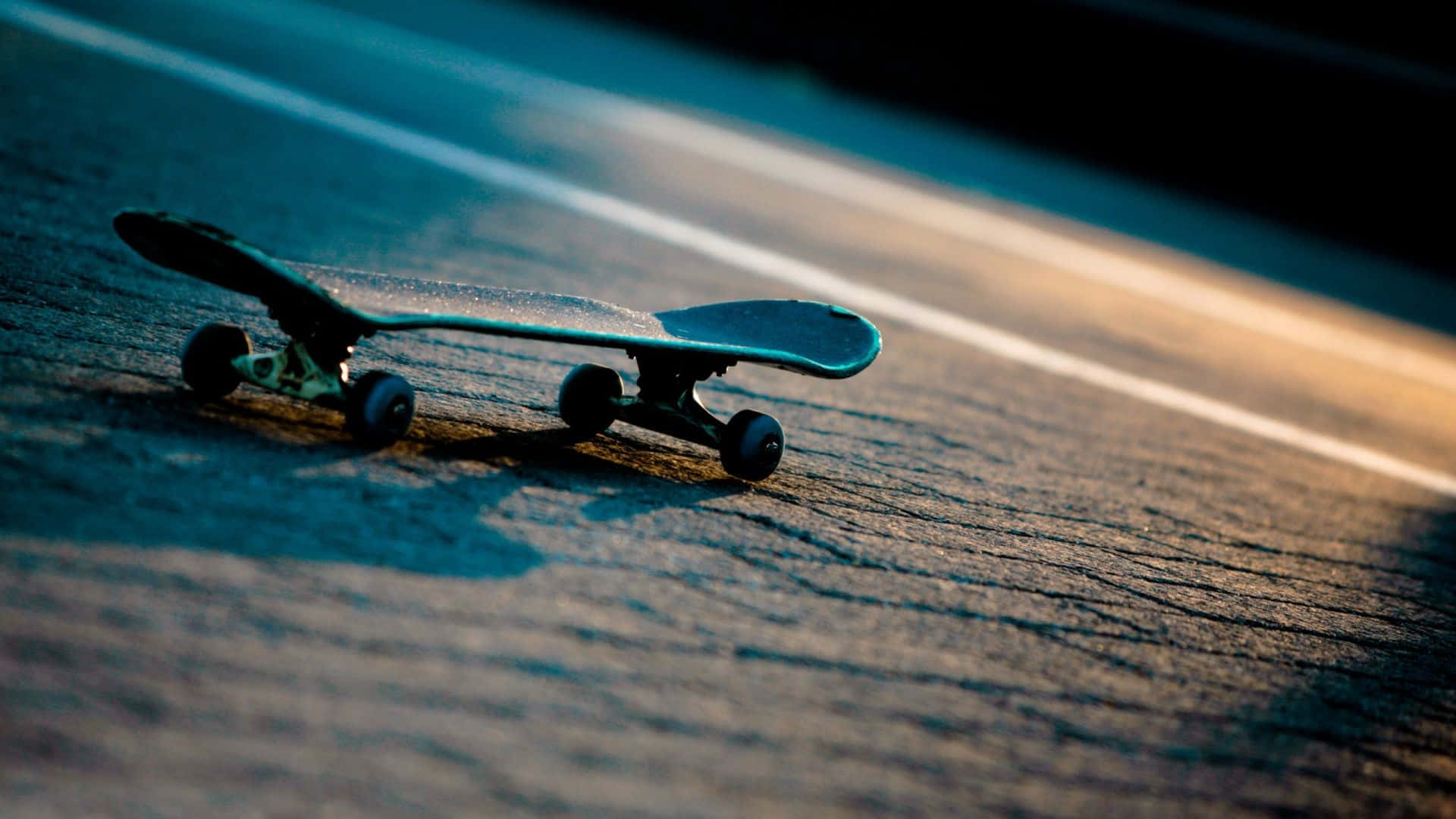 skateboarding 桌布 壁紙 — 一塊滑板放在陽光普照的瀝青路上，路上有白色線條，沐浴在溫暖的金色光芒中。