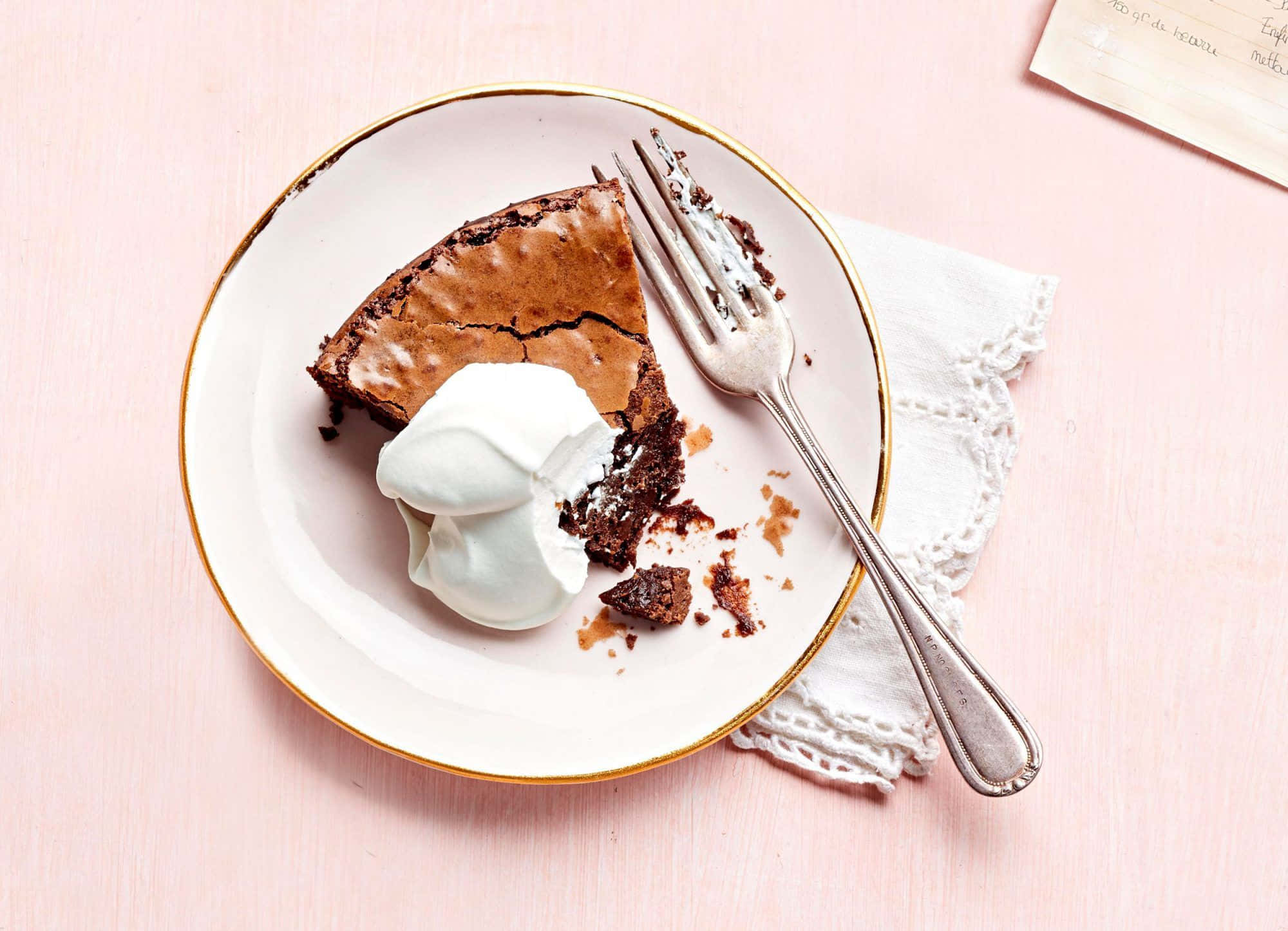 Winter Desserts 桌布 壁紙 — 一塊濃郁的巧克力布朗尼蛋糕，配上鮮奶油，放在金色邊盤上，置於粉紅色木質表面。