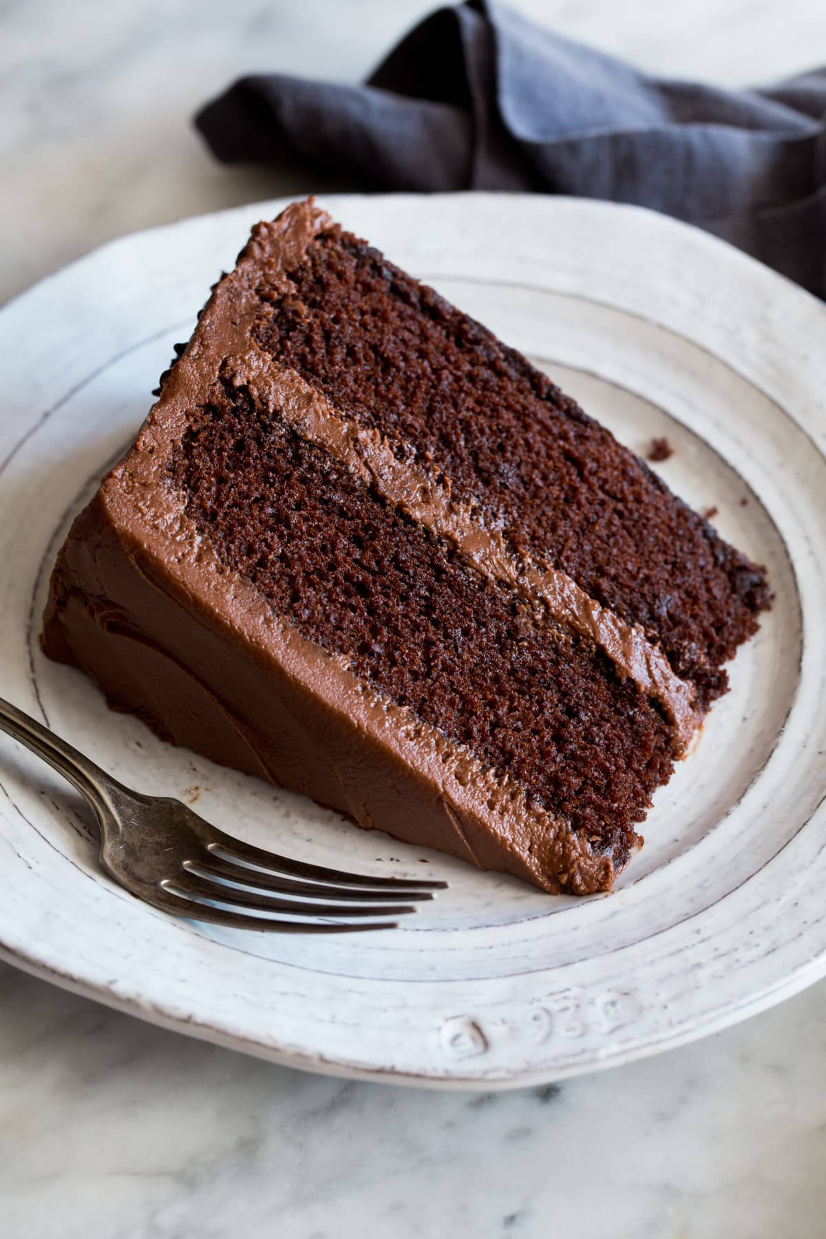 Chocolate Cake 桌布 壁紙 — 一塊濃郁的巧克力蛋糕，上面有厚厚的糖霜，放在一個樸素的白盤上，旁邊有一把叉子。