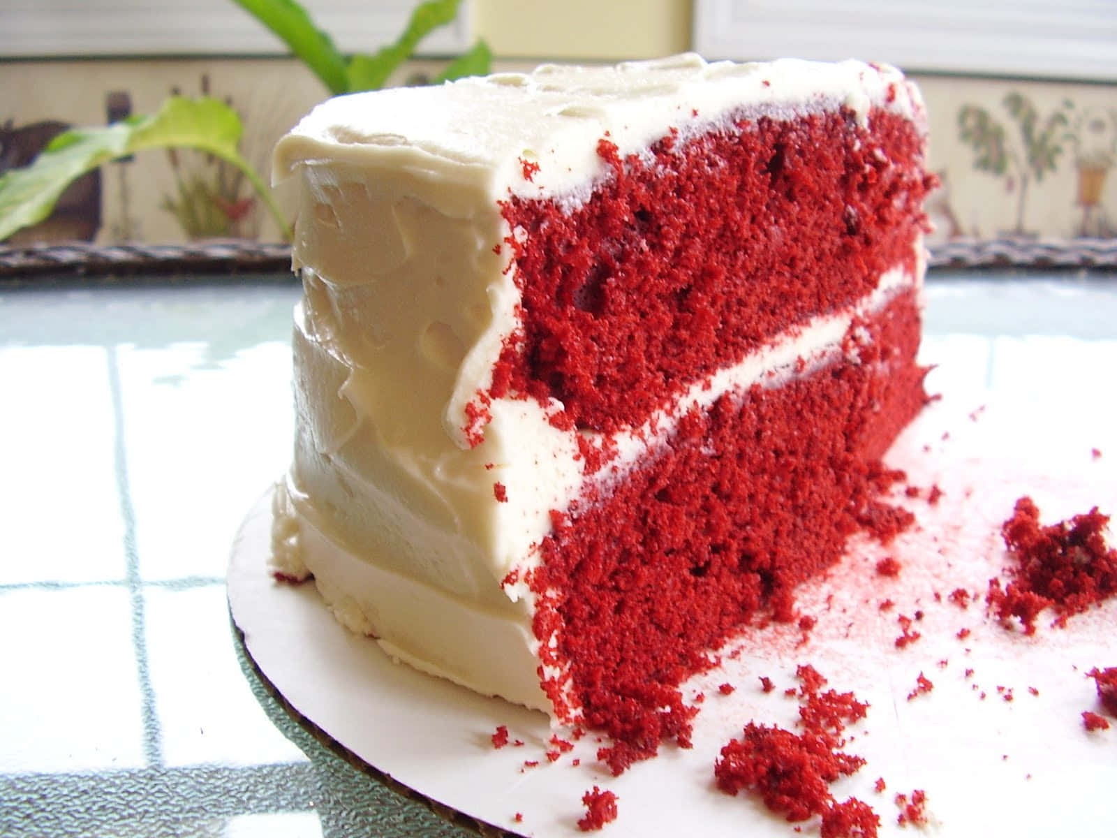 Red Velvet Cake 桌布 壁紙 — 一塊濃郁的紅絲絨蛋糕，配上 creamy 白色糖霜，放在盤子上，周圍散落著蛋糕碎。