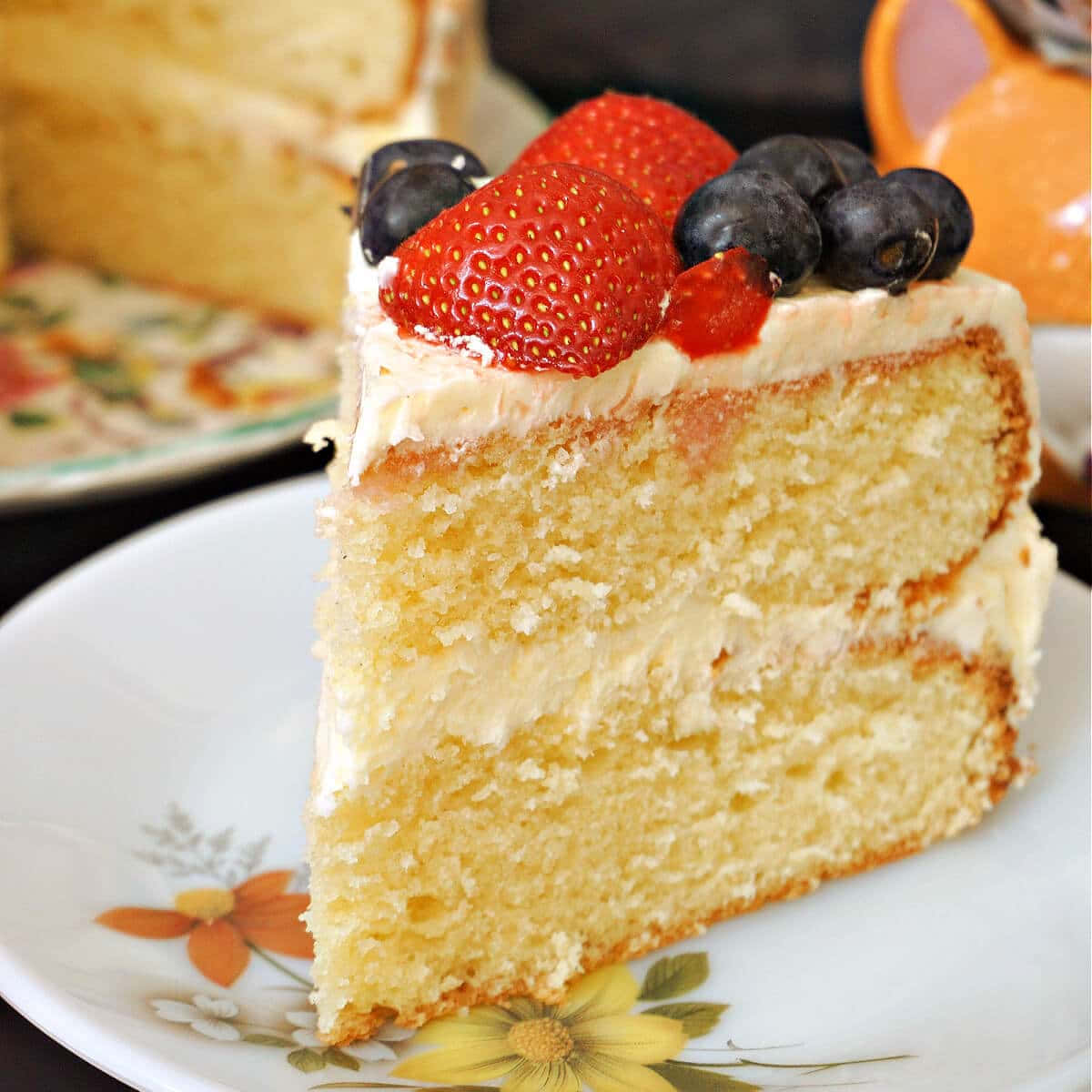 Buttercream 桌布 壁紙 — 一塊濕潤的層狀香草蛋糕片，上面放上新鮮草莓和藍莓，置於花卉圖案盤上。