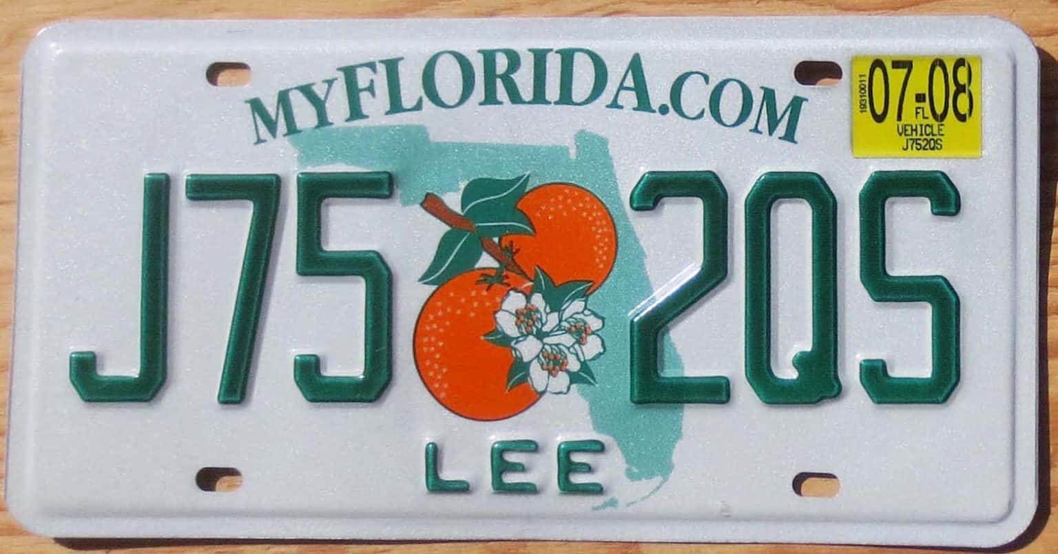 License Plate 桌布 壁紙 — 一塊白色佛羅里達車牌，帶有綠色字體和橙花圖案，放置在木質表面上。