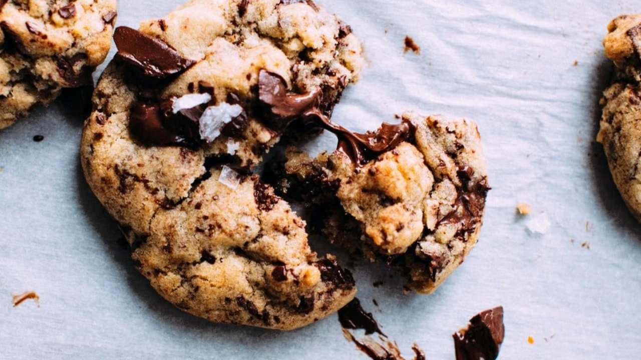720p Cookies 桌布 壁紙 — 一塊破碎的巧克力餅乾的特寫，露出黏稠的融化巧克力和烘焙紙上的片狀海鹽。