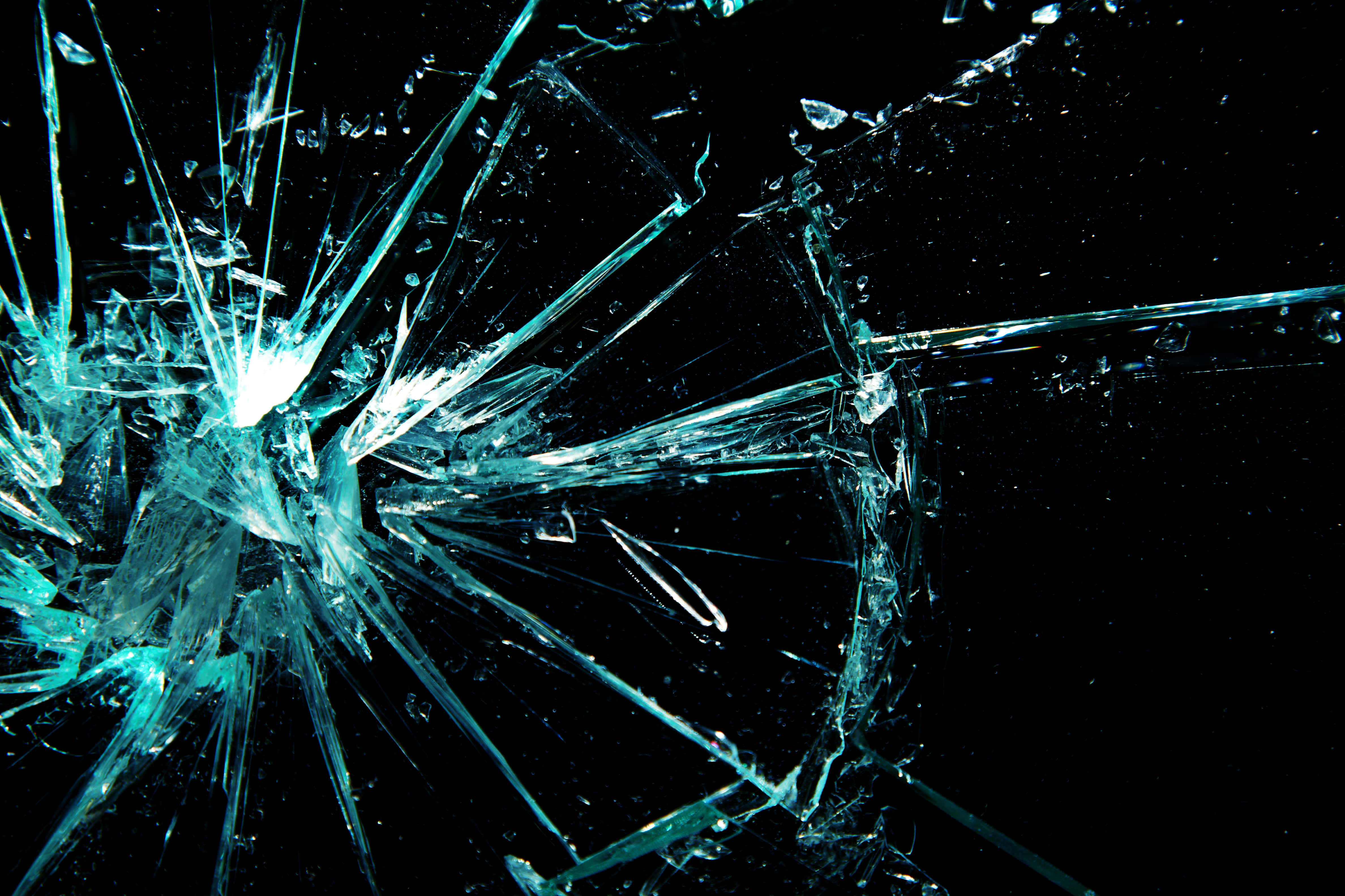 Fracture Glass 桌布 壁紙 — 一塊破碎的玻璃板，帶有尖銳的藍綠色碎片，從明亮的中央撞擊點向黑色背景輻射。