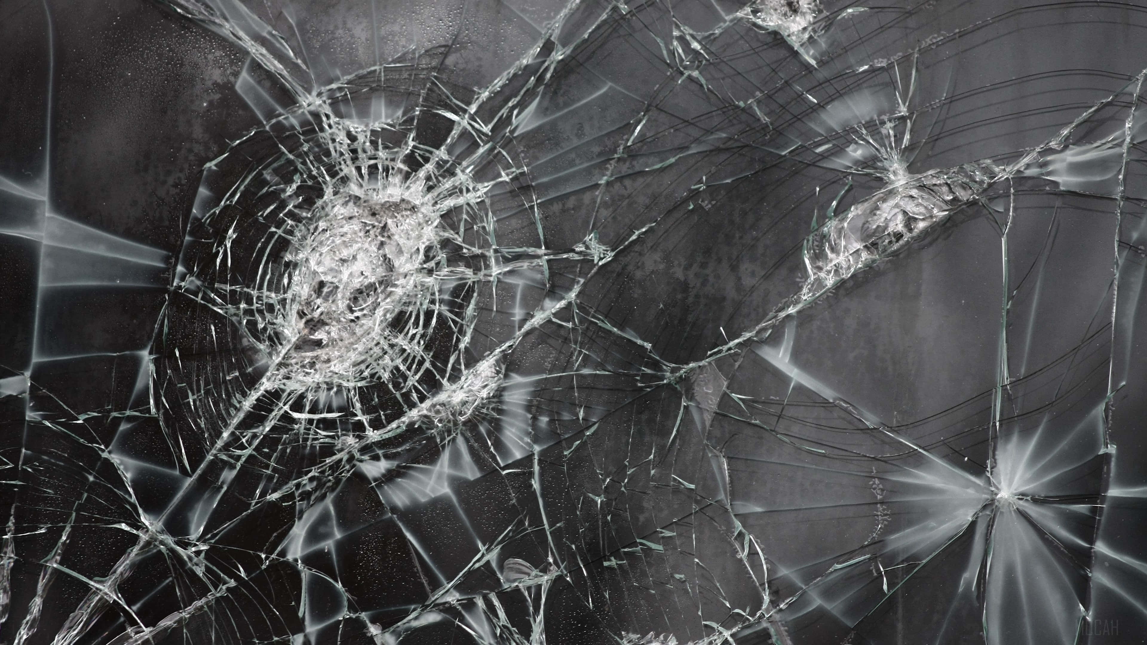 Fracture Glass 桌布 壁紙 — 一塊破碎的玻璃表面，在深灰色背景上從撞擊點散發出複雜的裂紋。