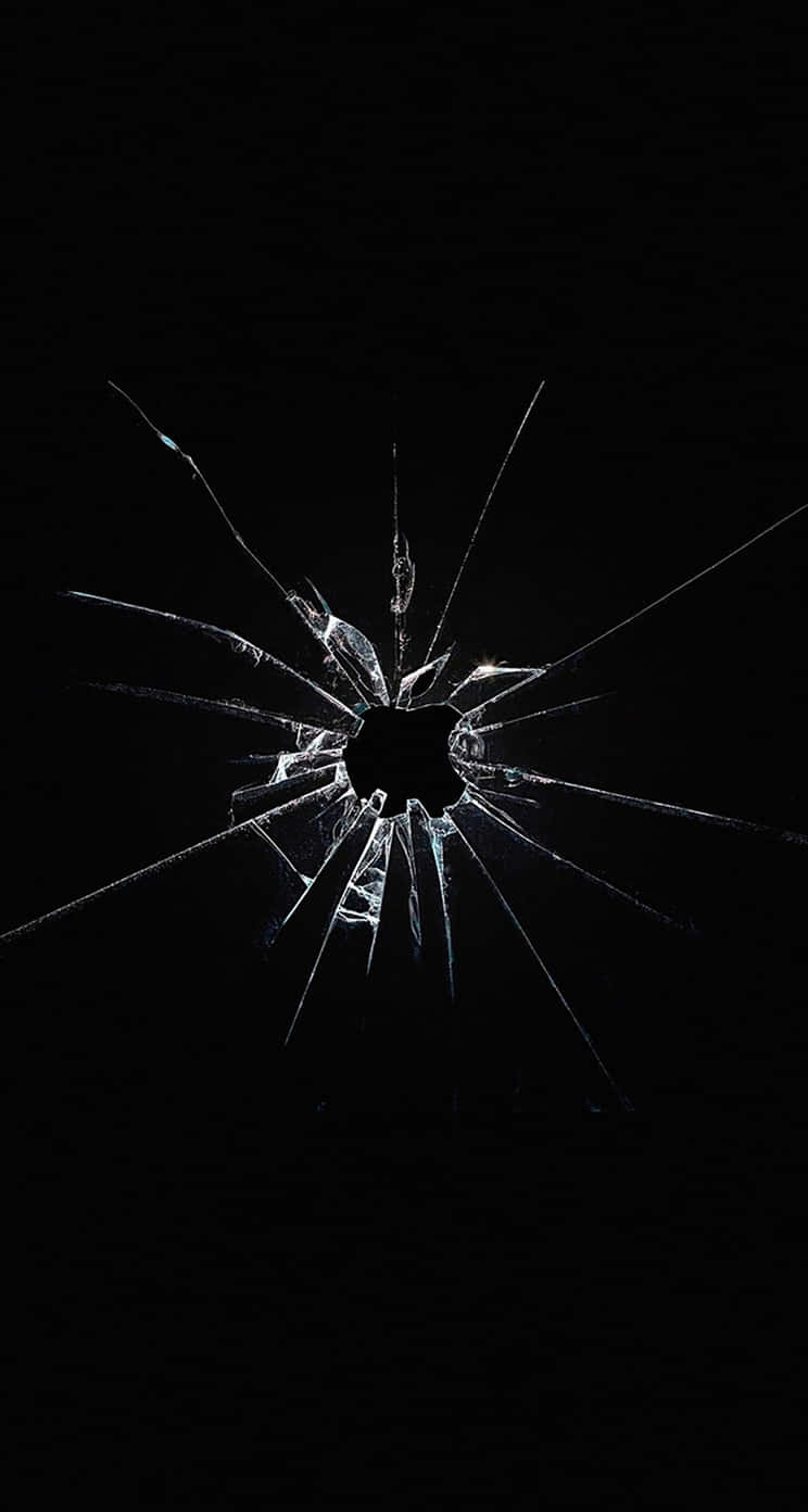 Broken Glass 桌布 壁紙 — 一塊破碎的玻璃表面，從中央孔洞放射出尖銳裂紋，背景為純黑色。